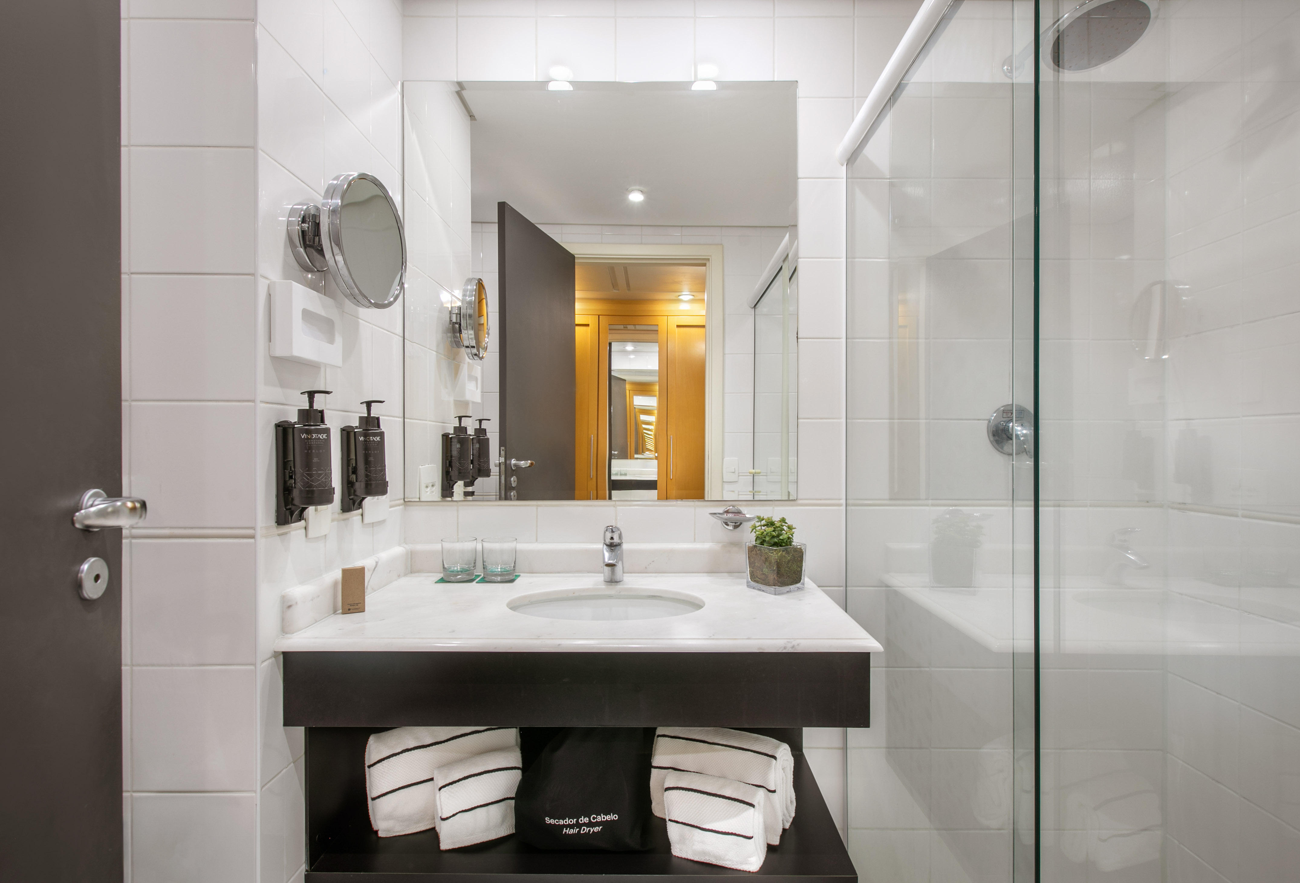 Modern white tiled bathroom with vanity, sink, mirror, and glass shower.