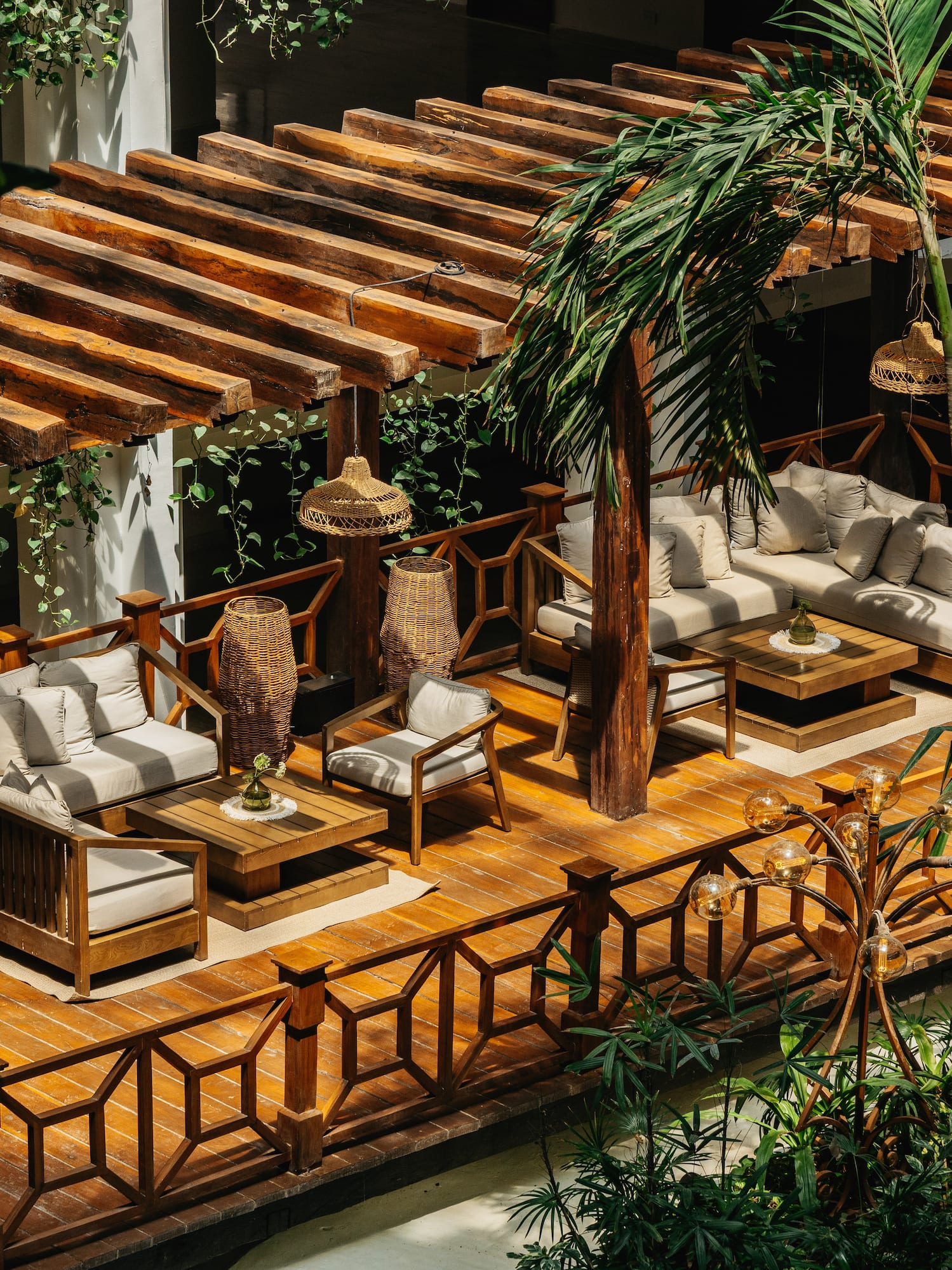 Tropical resort lounge with wooden pergola, sofas, and lush plants.