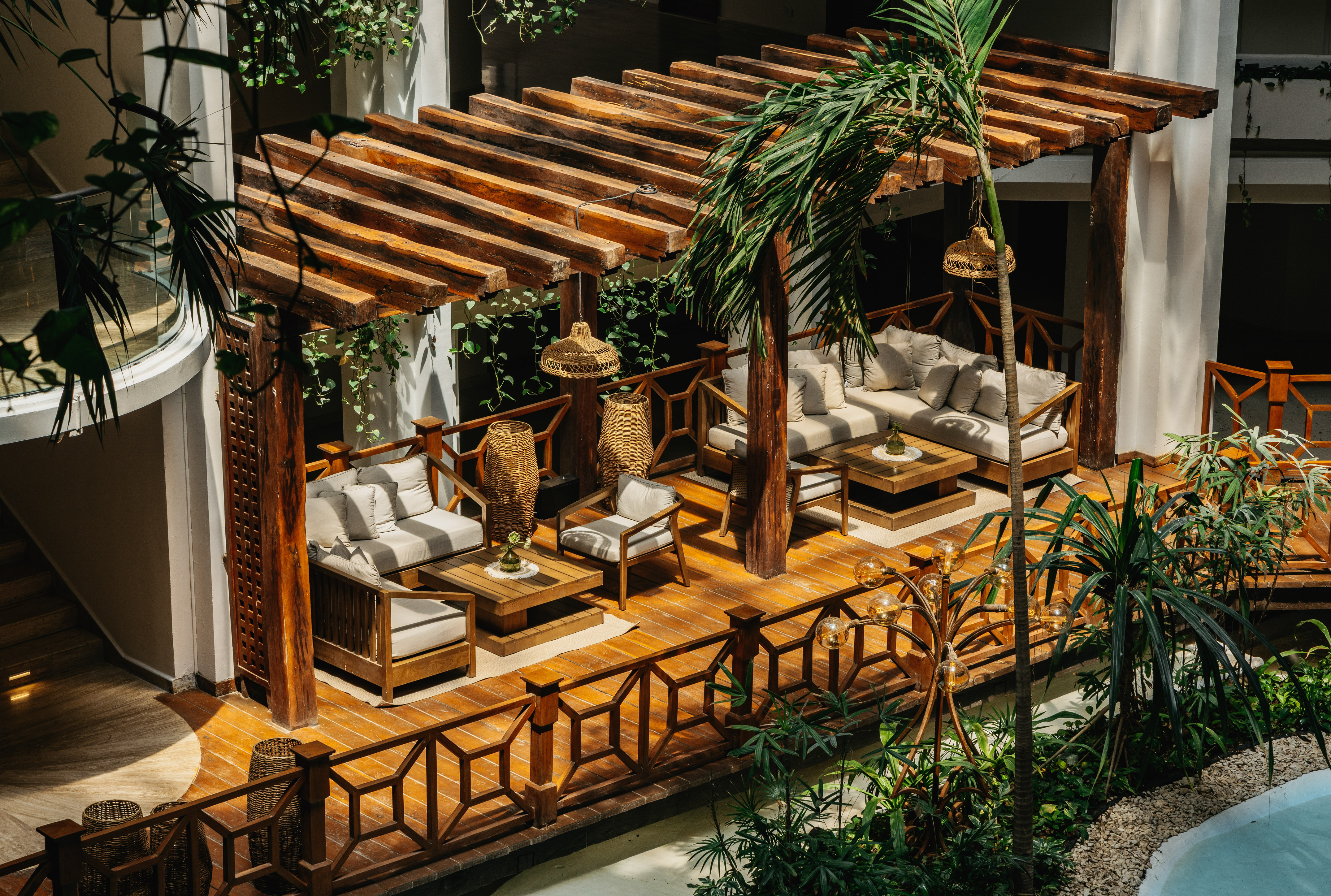 Tropical resort lounge with wooden pergola, sofas, and lush plants.
