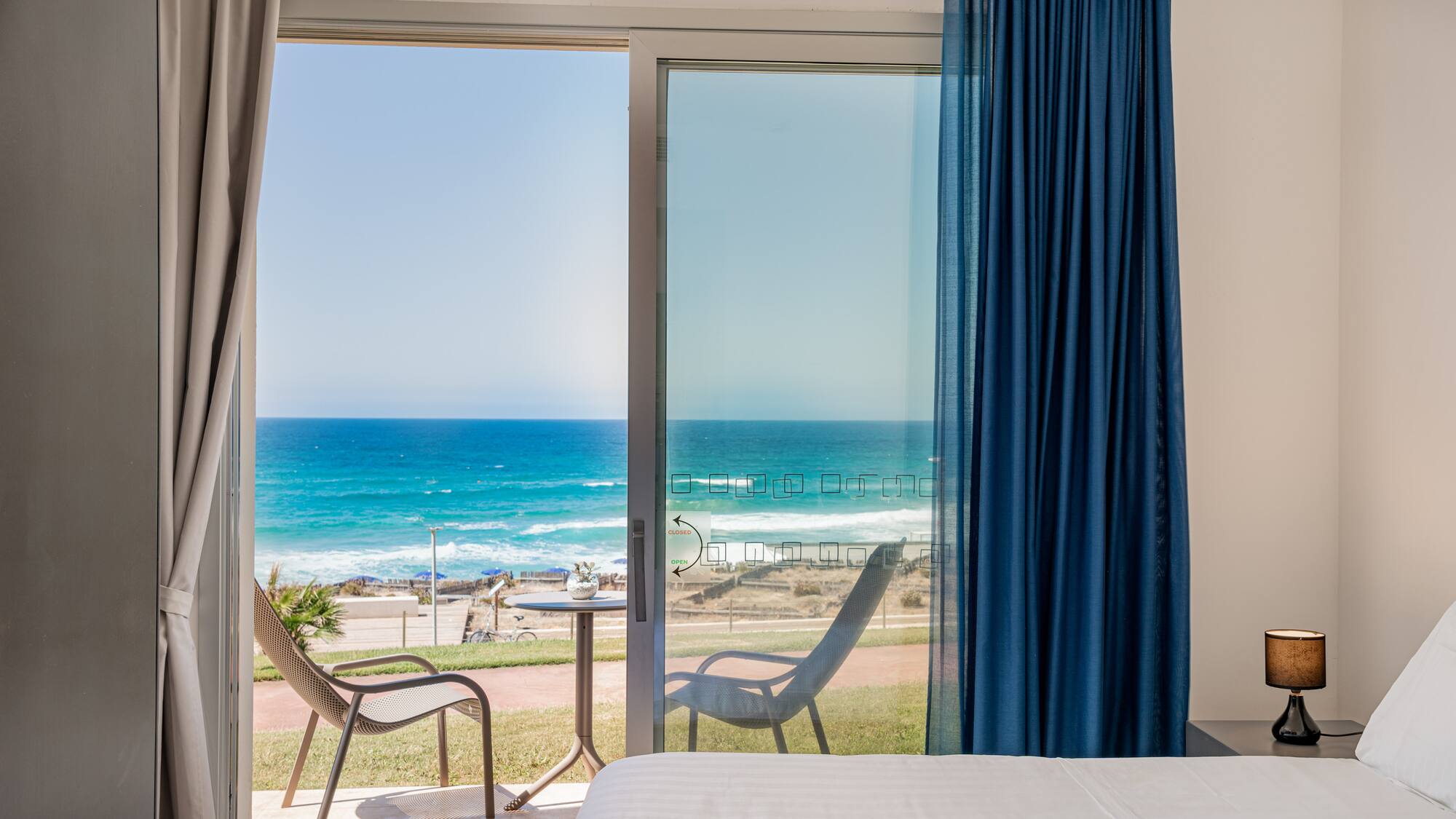 a room with a bed and chairs and a beach view
