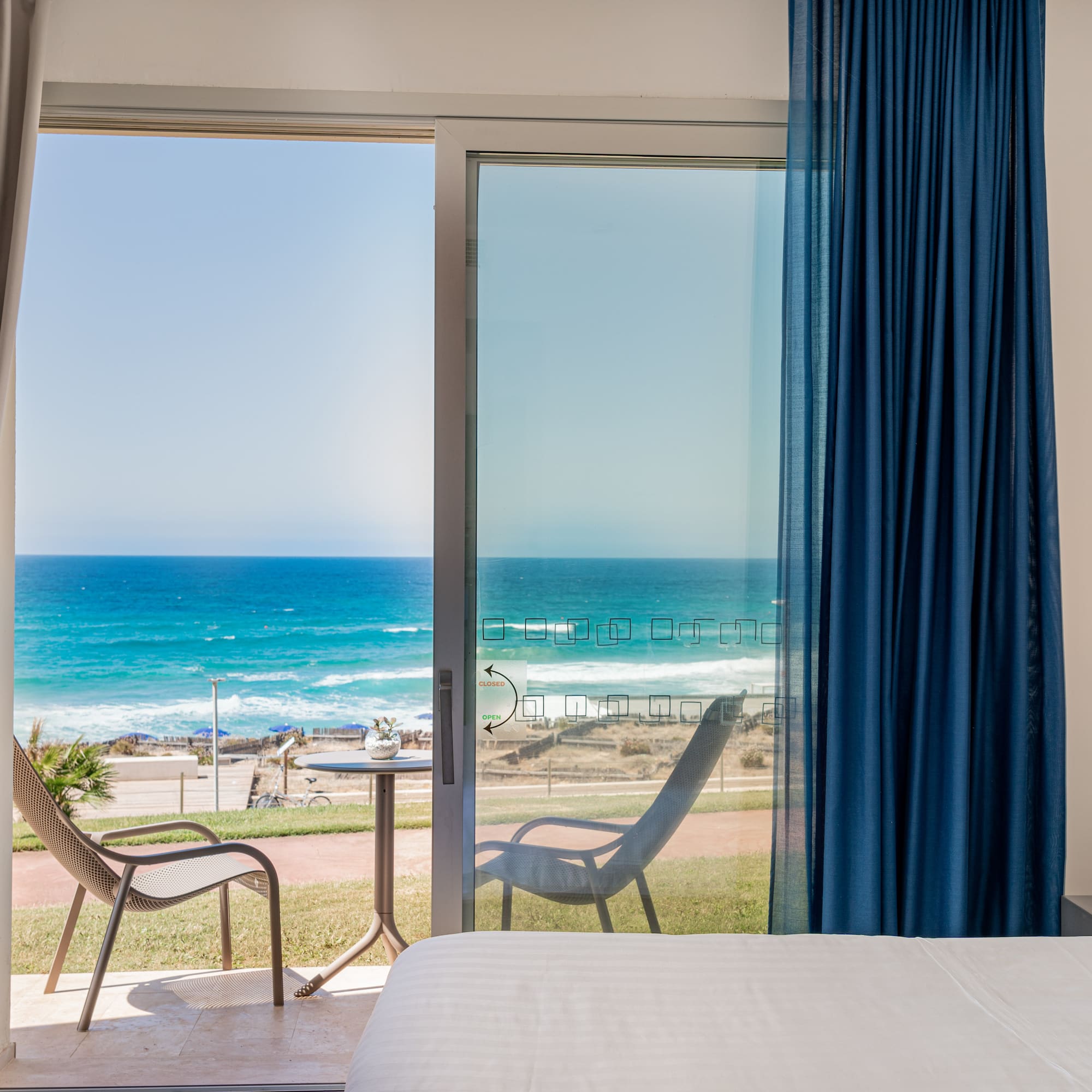 a room with a bed and chairs and a beach view