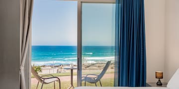 a room with a bed and chairs and a beach view