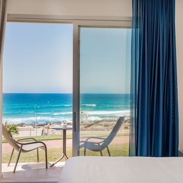 a room with a bed and chairs and a beach view