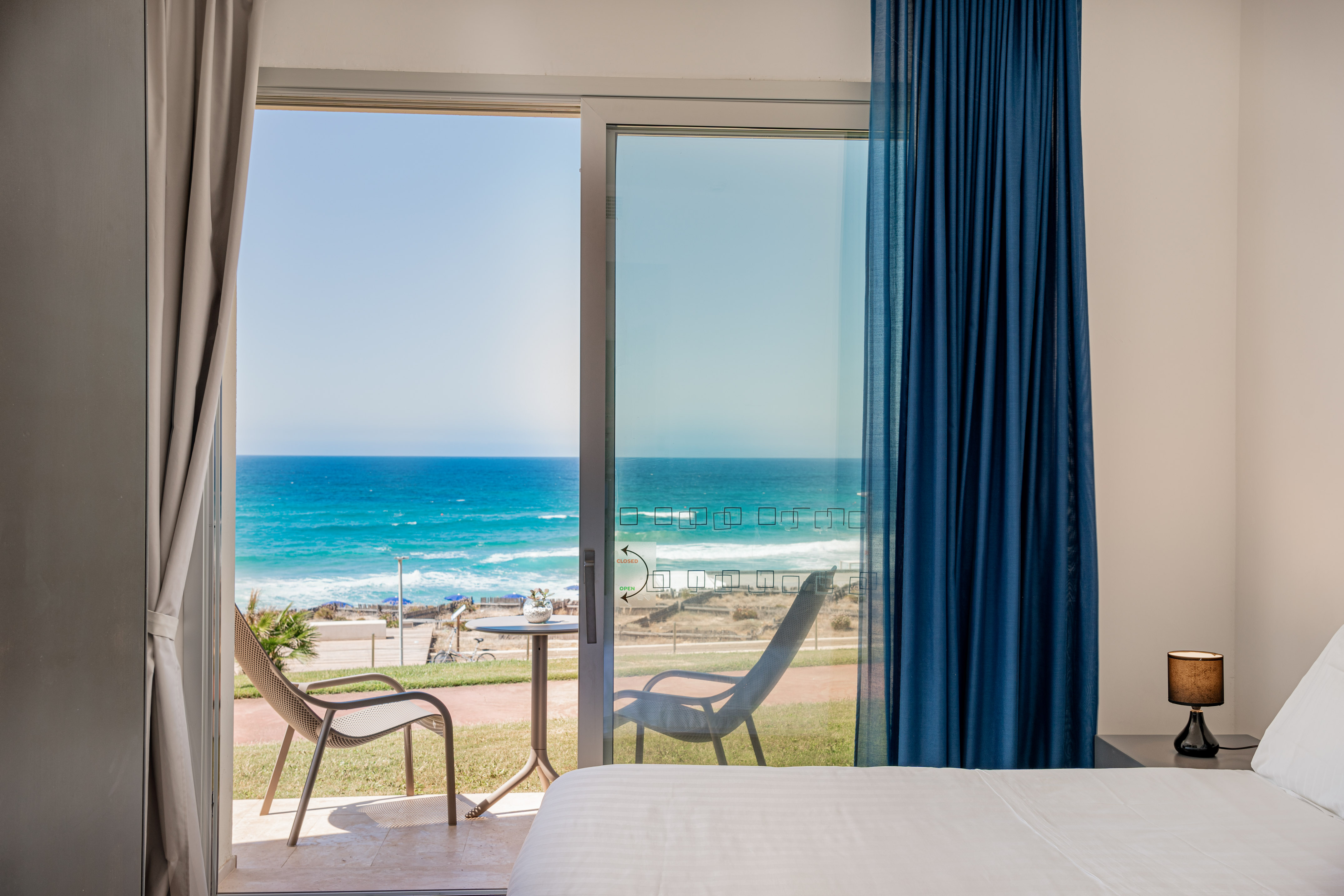 Beachfront hotel room with ocean view balcony and patio chairs.