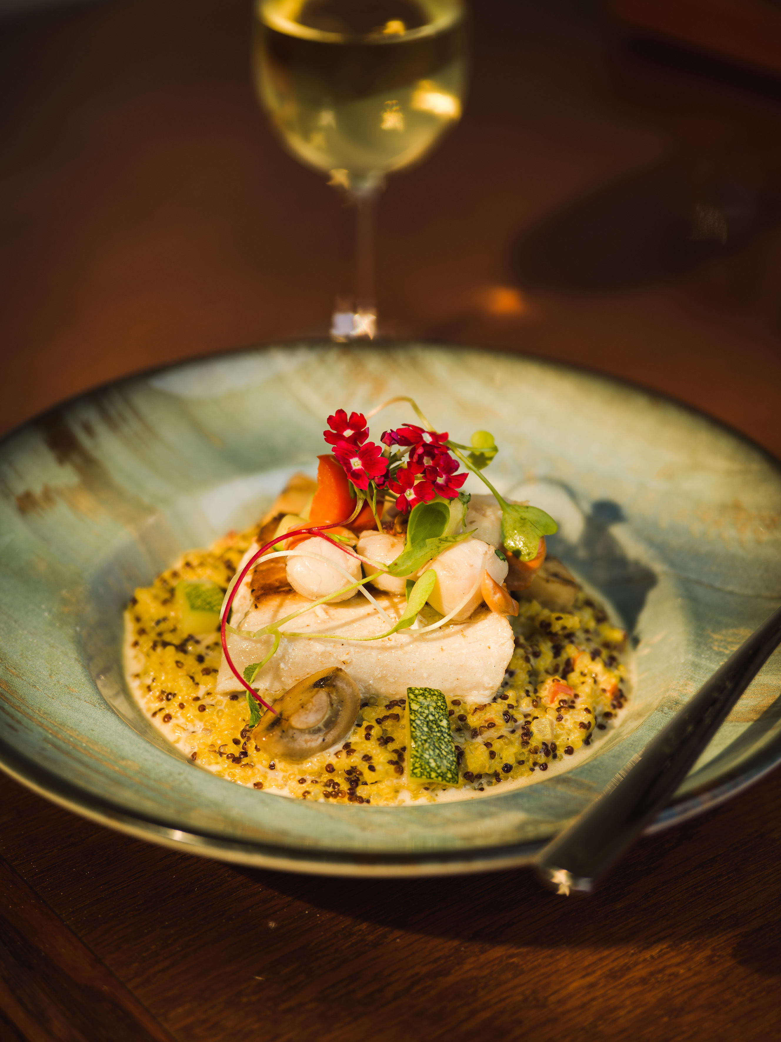Gourmet fish and scallop dish with quinoa, vegetables, and white wine.