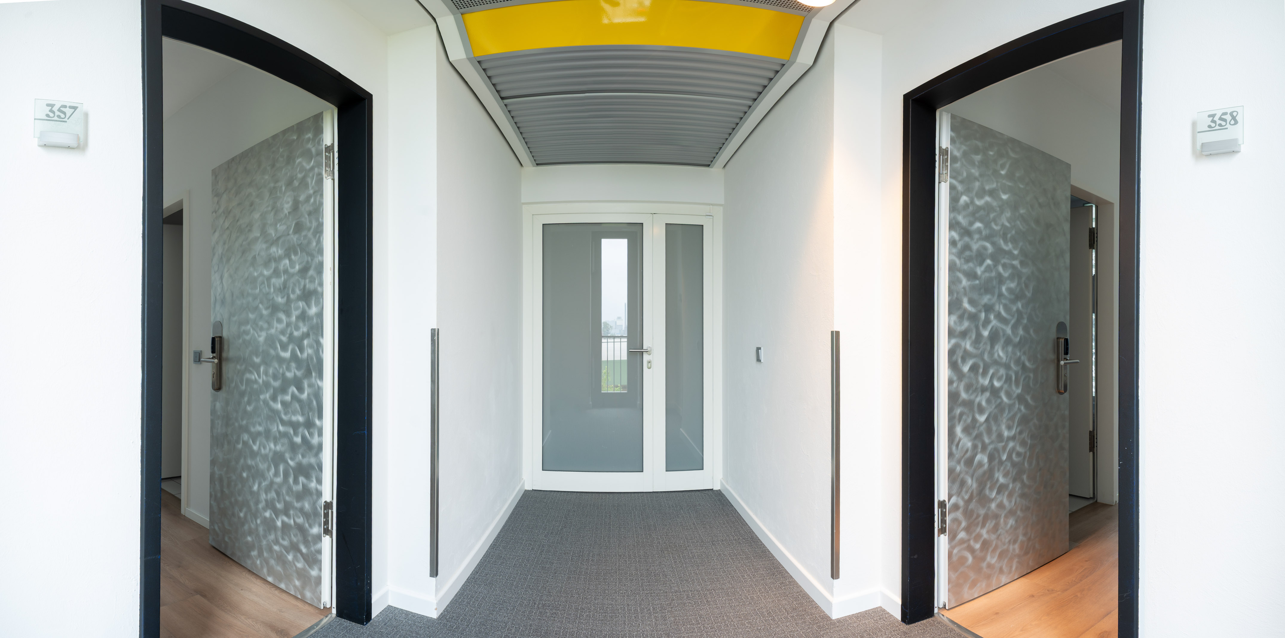 Modern hotel corridor with textured metallic doors and glass exit.