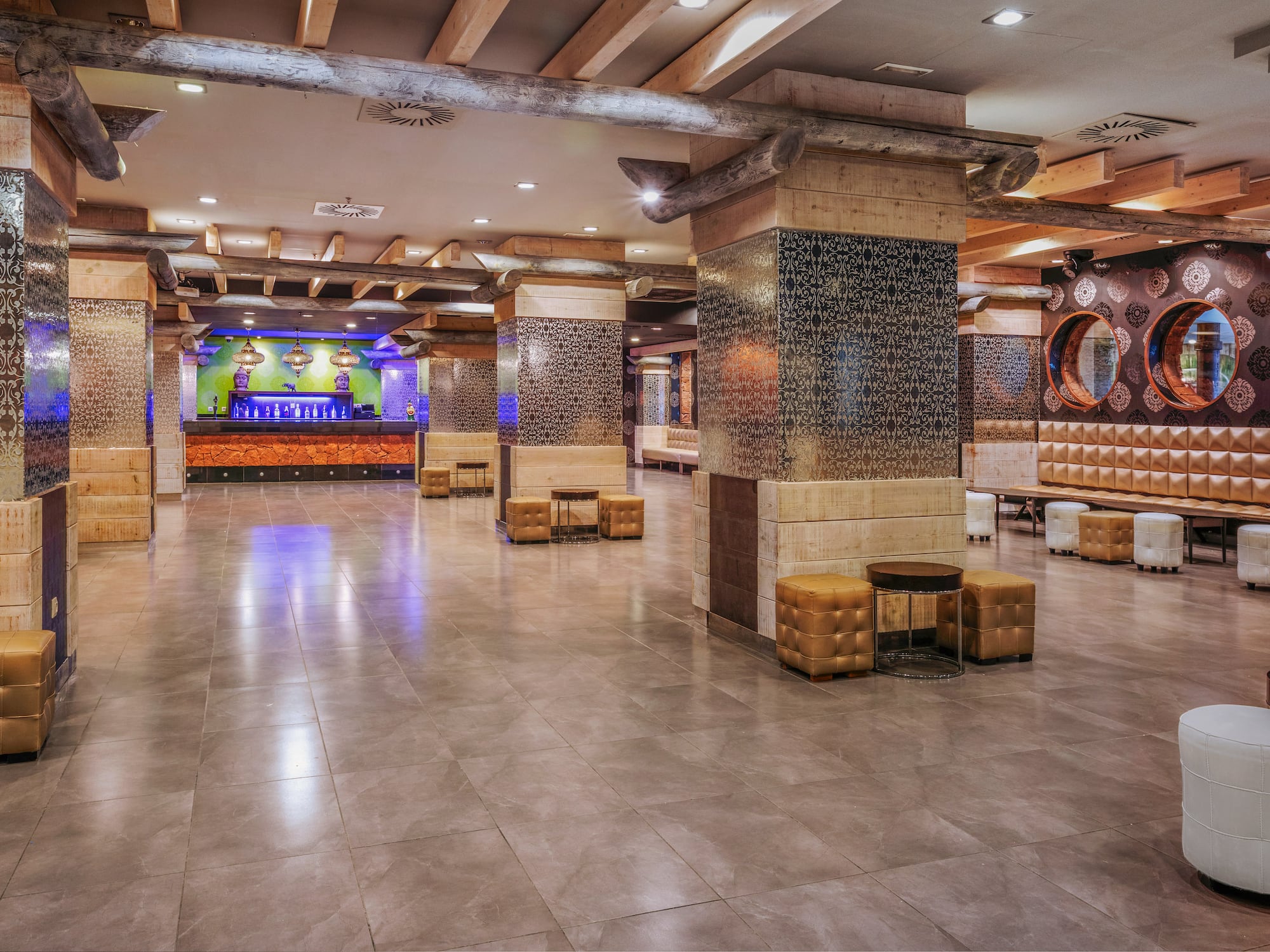 Hotel lobby bar with ornate columns, rustic wooden beams, and various seating.