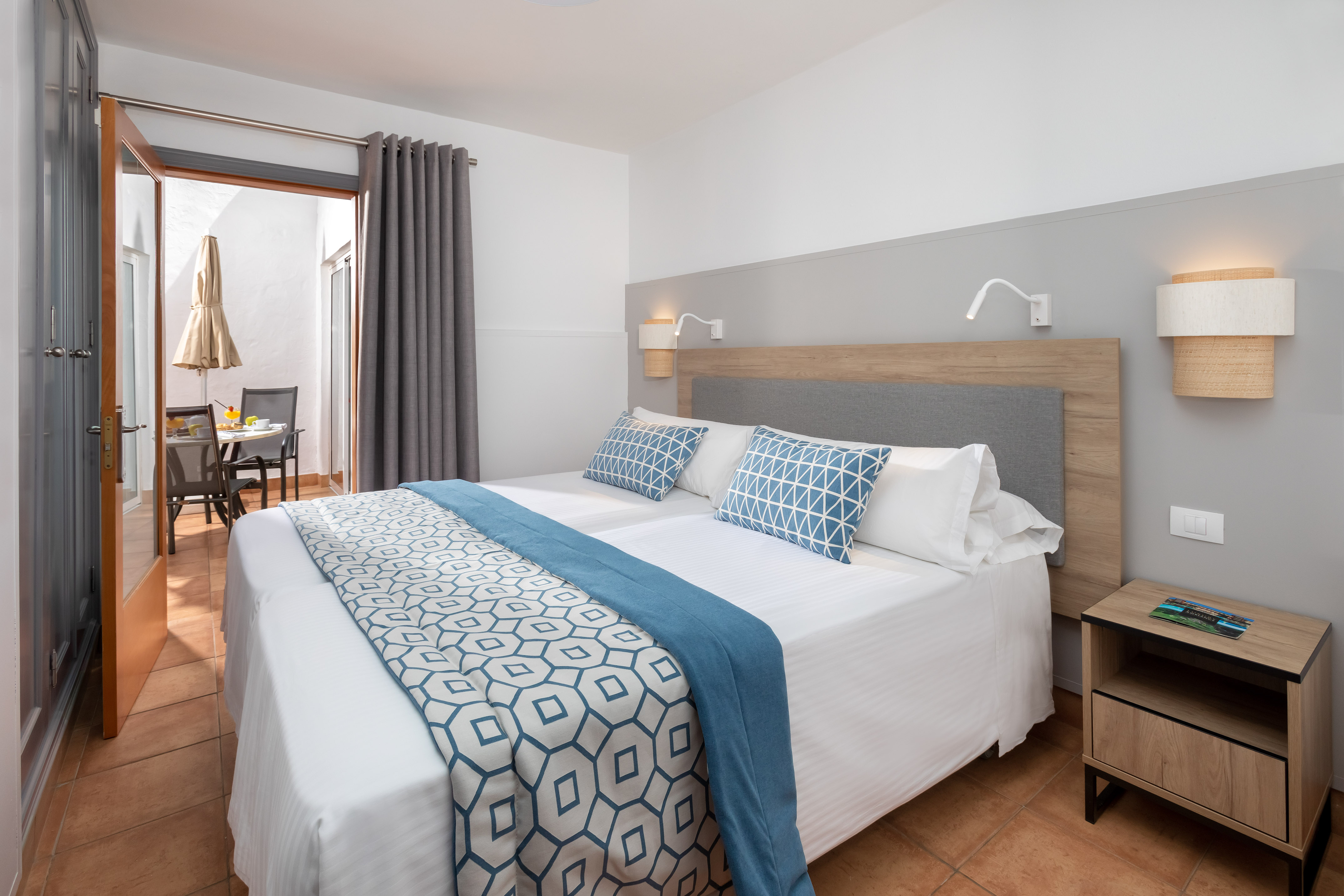 Hotel bedroom with twin beds, blue decor, and private patio dining area.