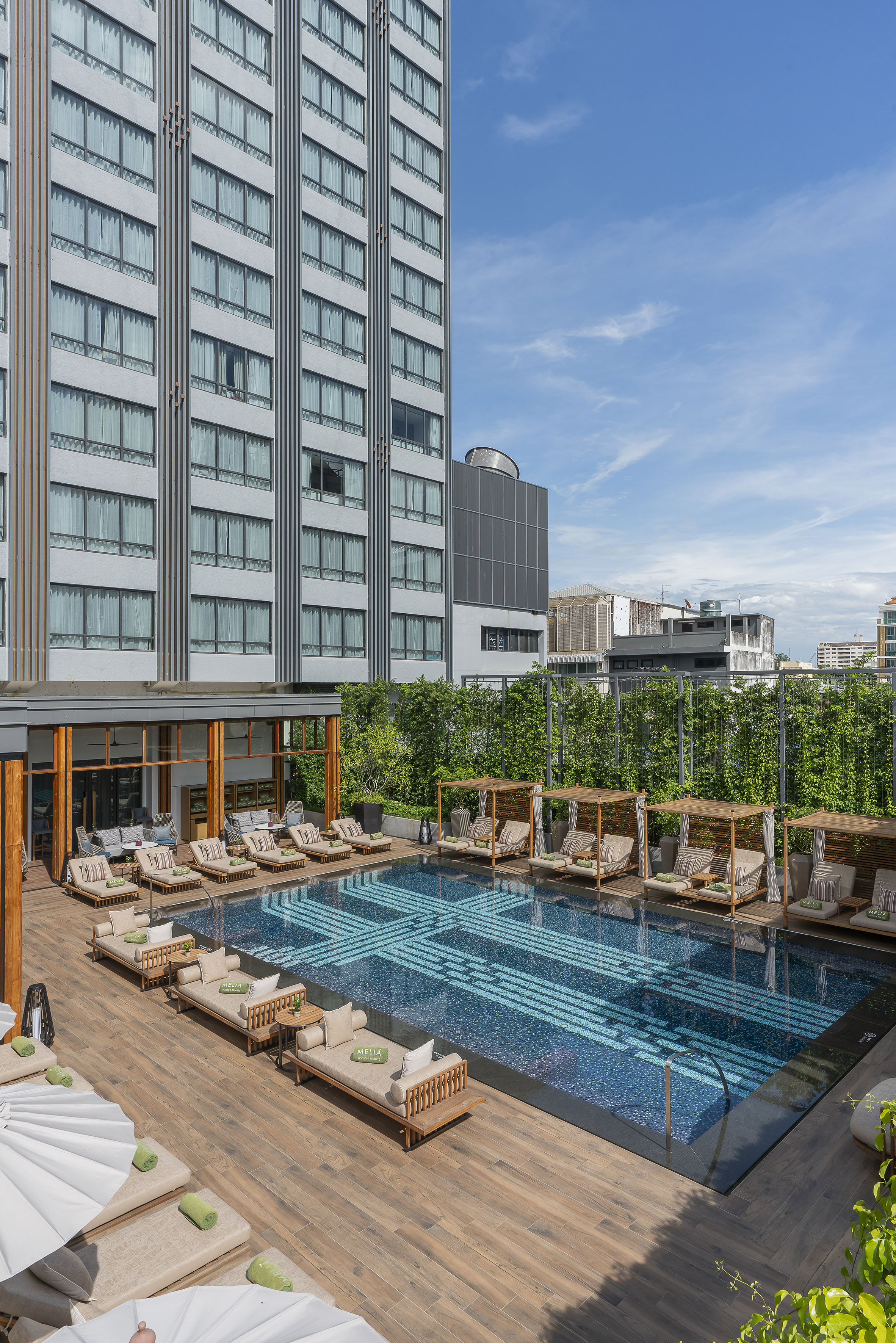 Modern hotel pool deck with patterned blue tiles, sun loungers, and cabanas.