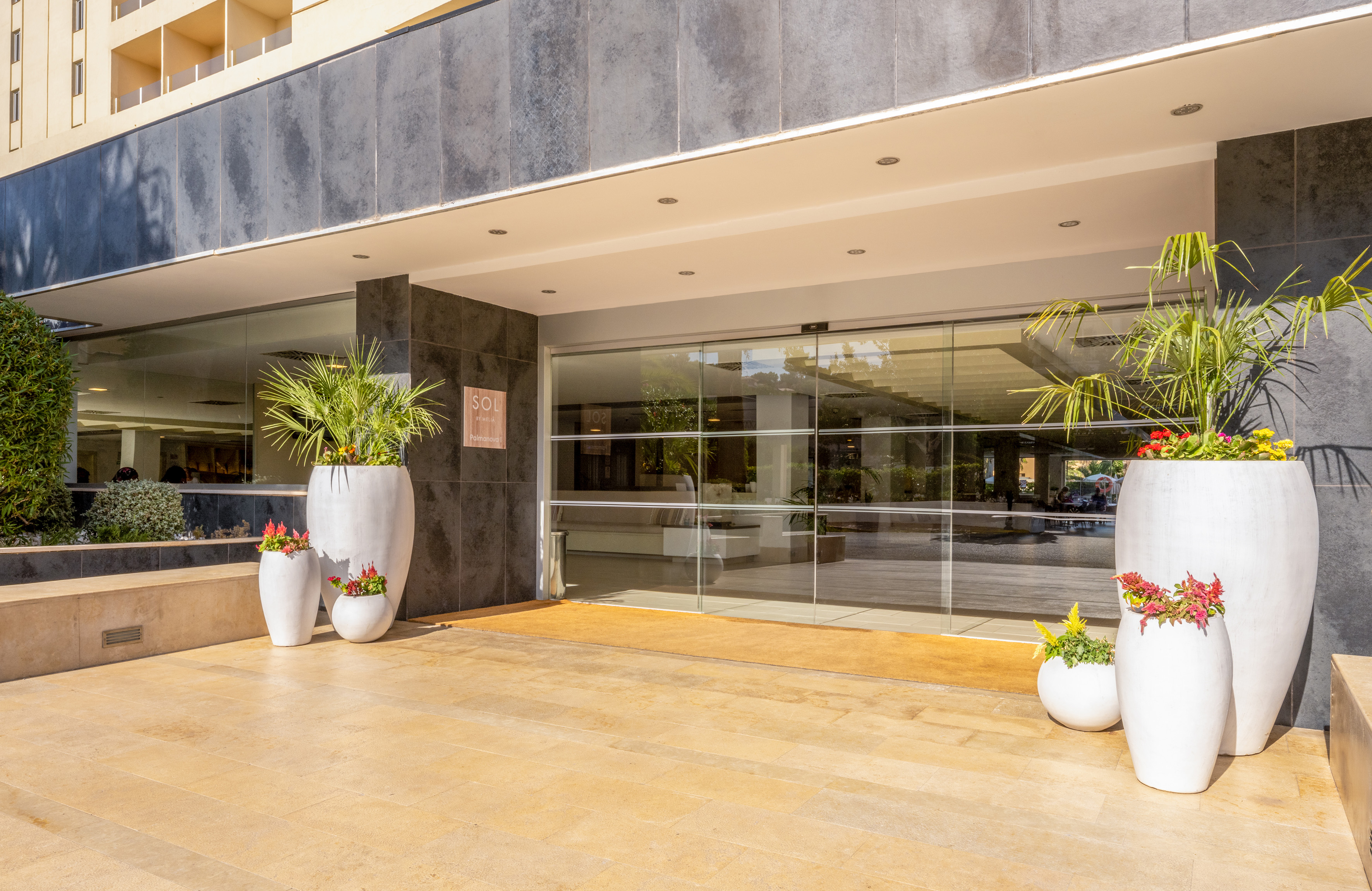 Sol Palmanova hotel entrance with glass doors, white planters, and lush greenery.