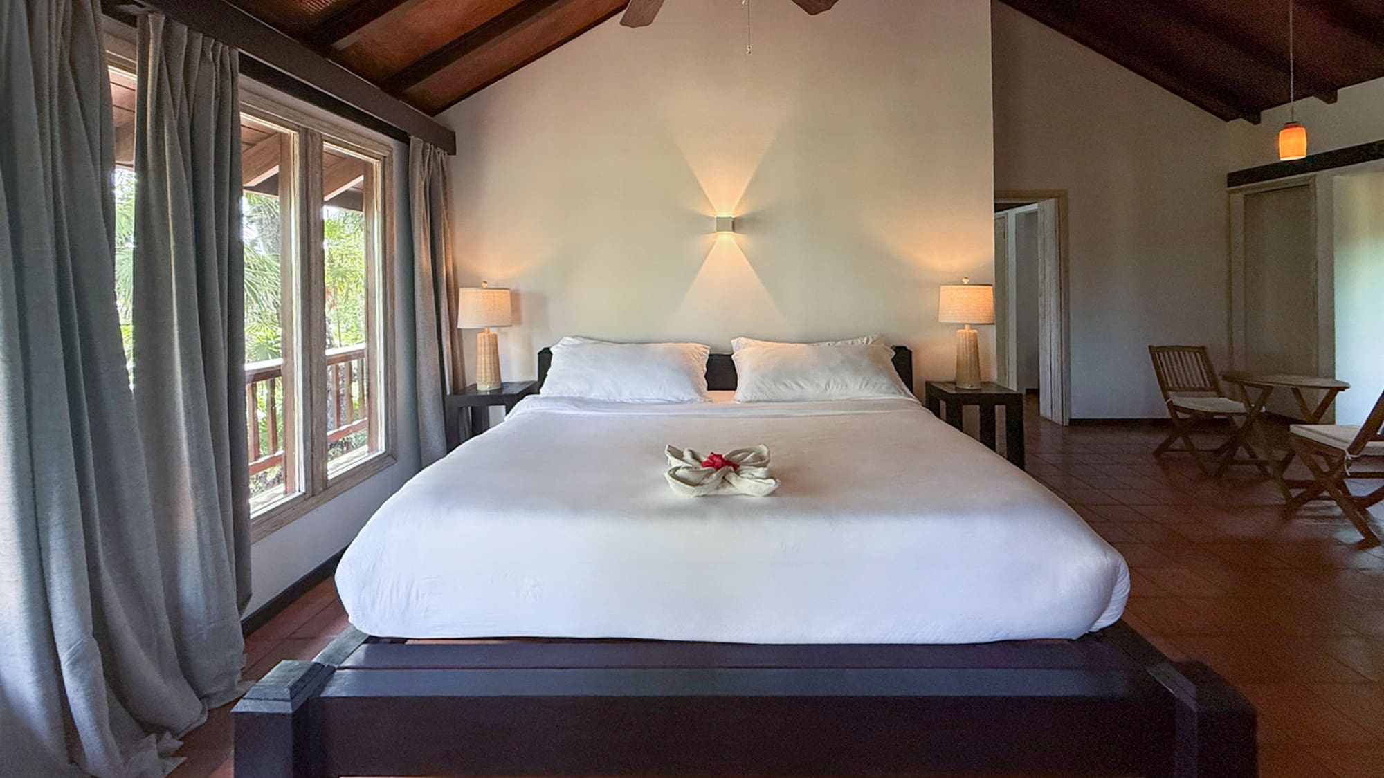 Rustic tropical bedroom with vaulted wood ceiling, queen bed, and balcony view.
