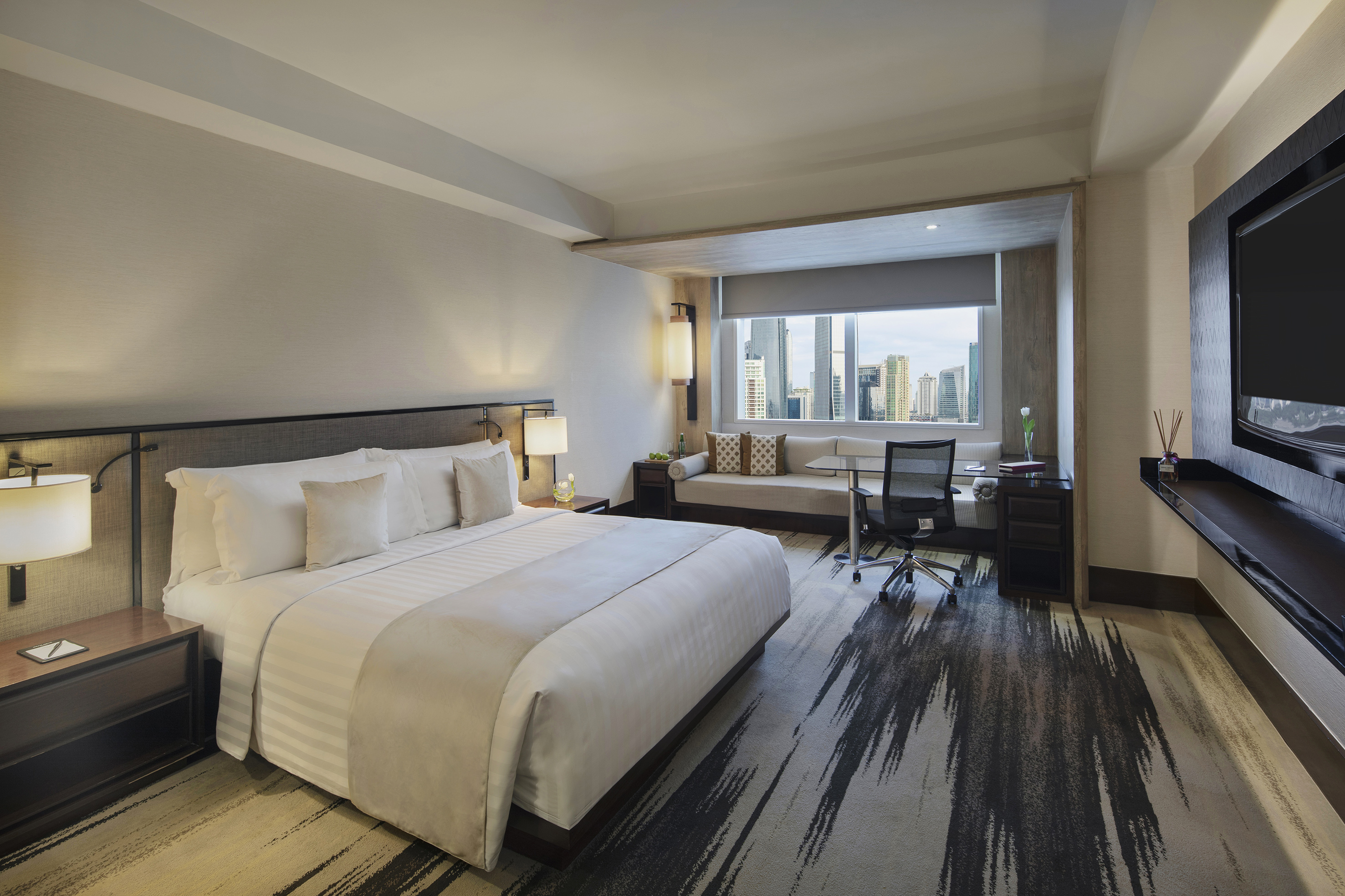 Modern hotel room with king bed, city view window, desk, and sofa.