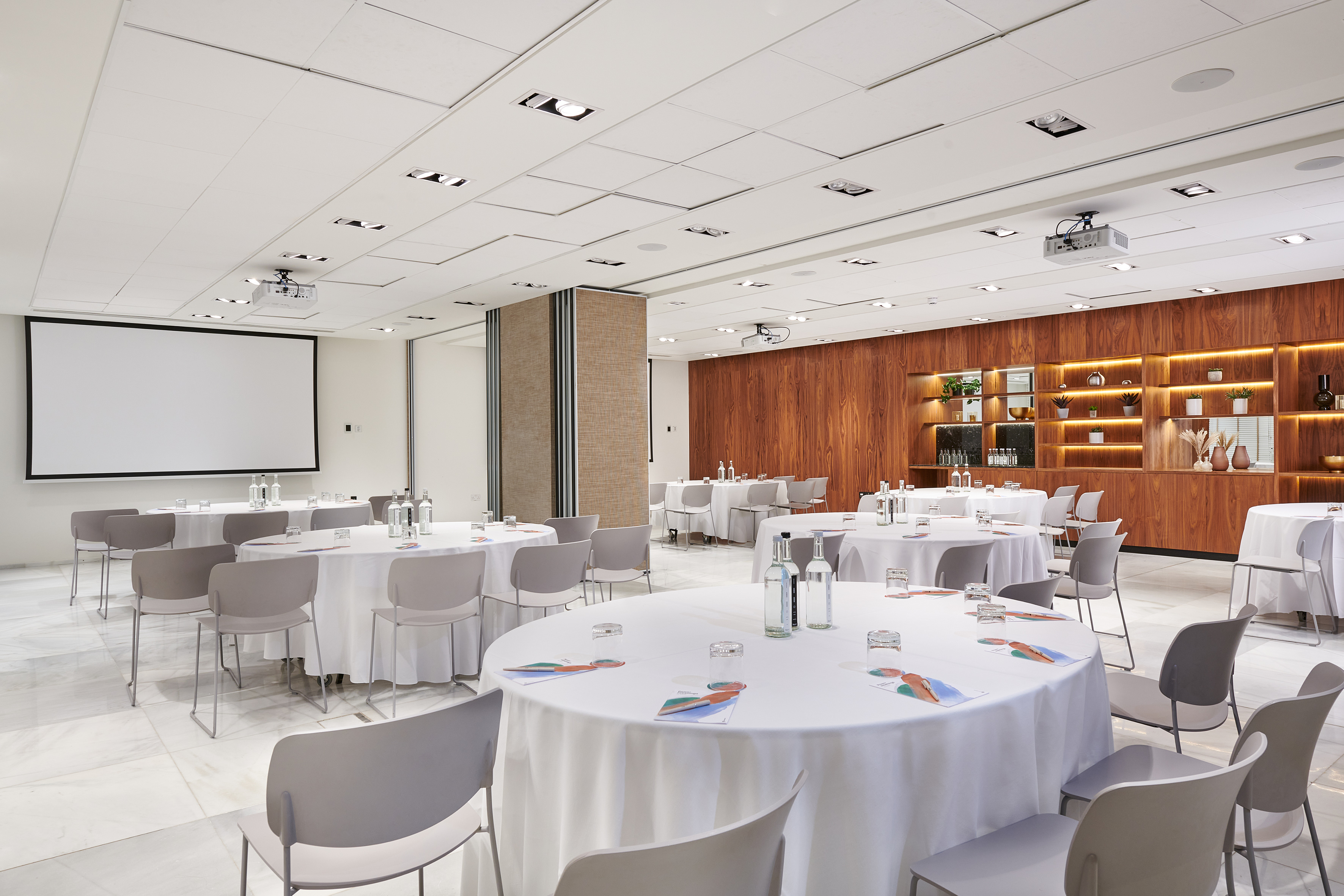 Modern meeting room with round tables, projector screen, and wood feature wall.