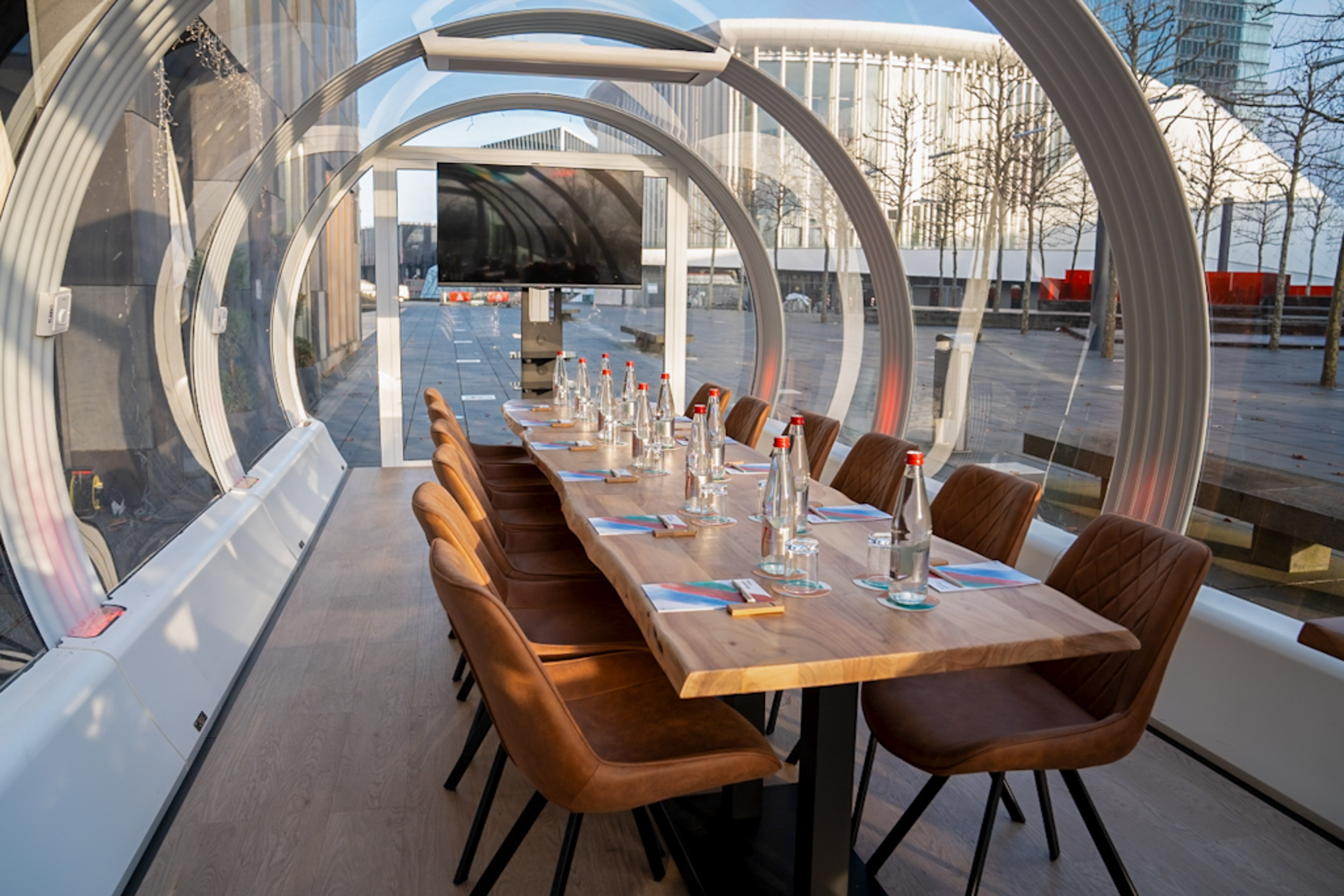 Outdoor conference pod with long wood table, brown chairs, and city view.