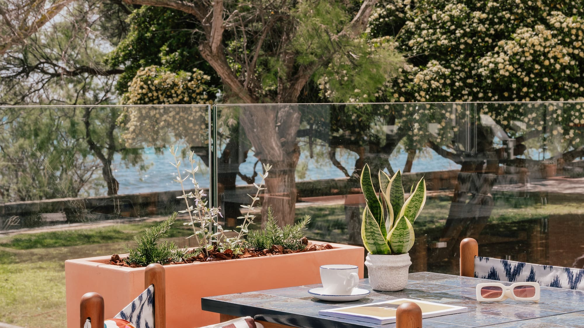 Resort patio dining area with sea view, blue table, wooden chairs, and plants.