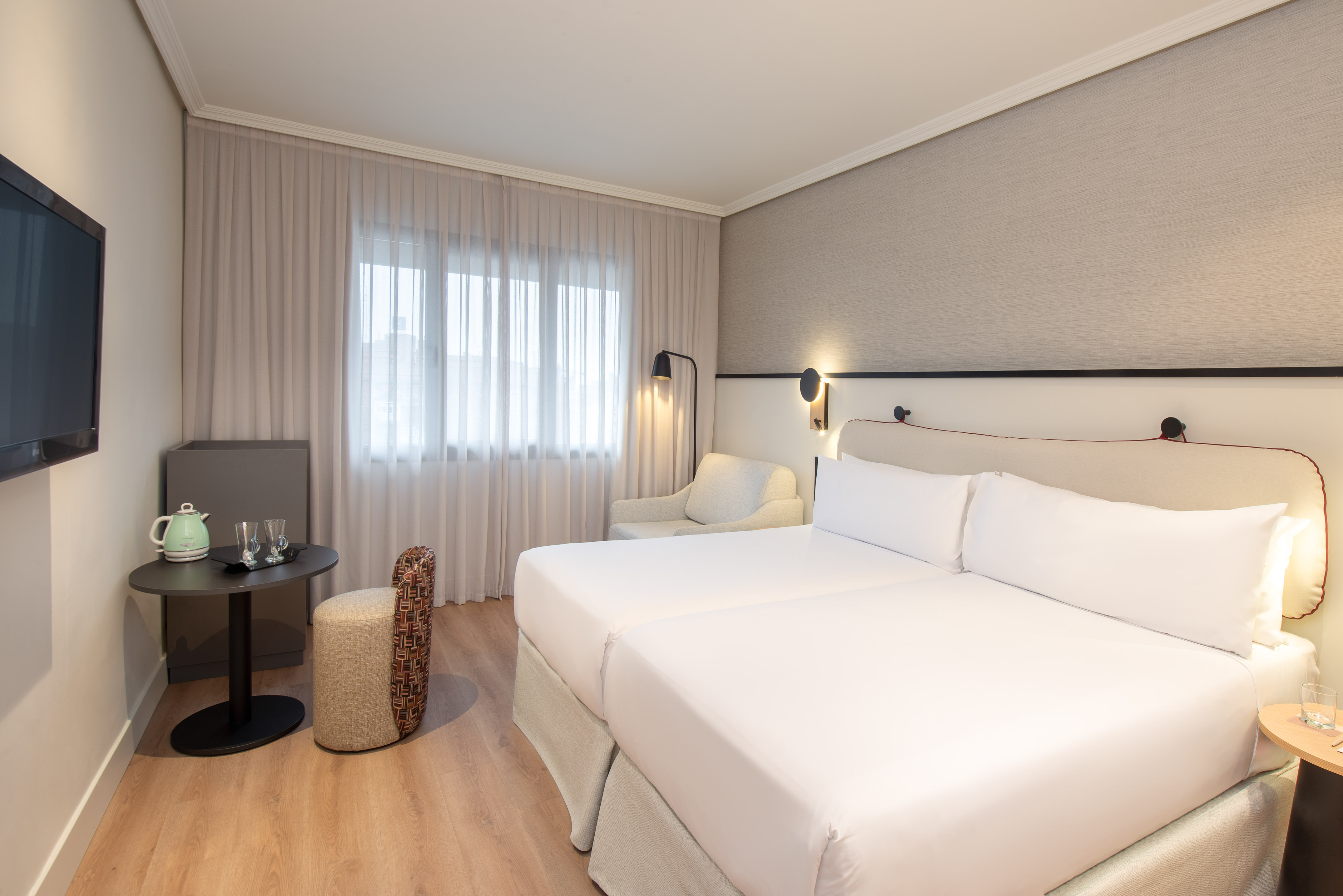 Modern hotel room with twin beds, TV, and wood floor.