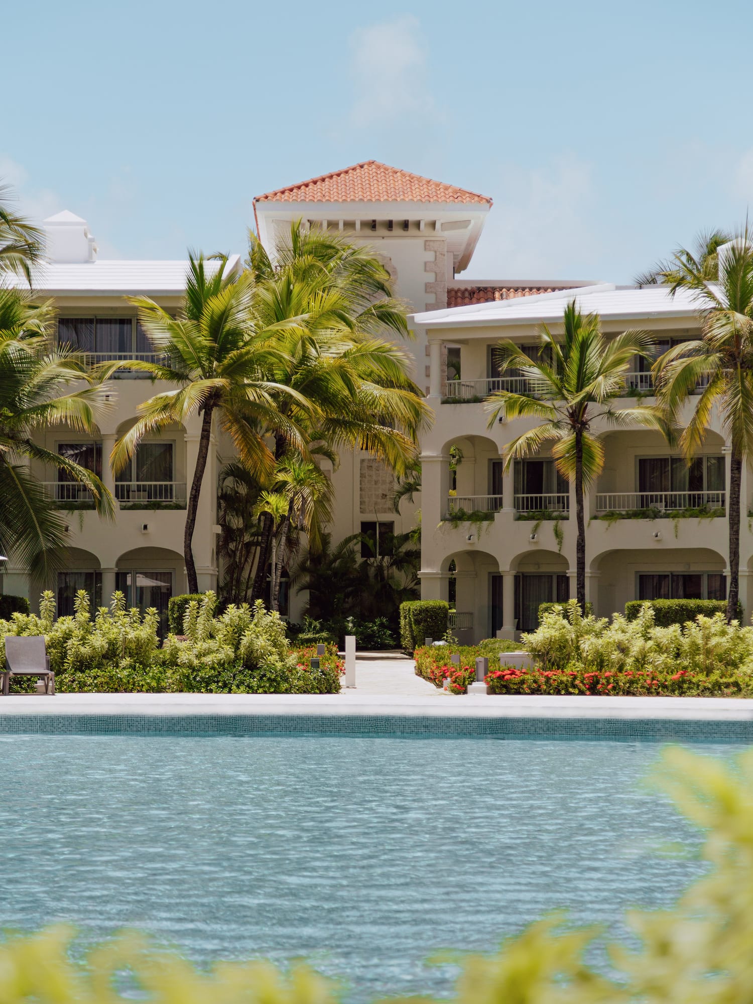 Tropical resort with white building, red roof, palm trees, and swimming pool.
