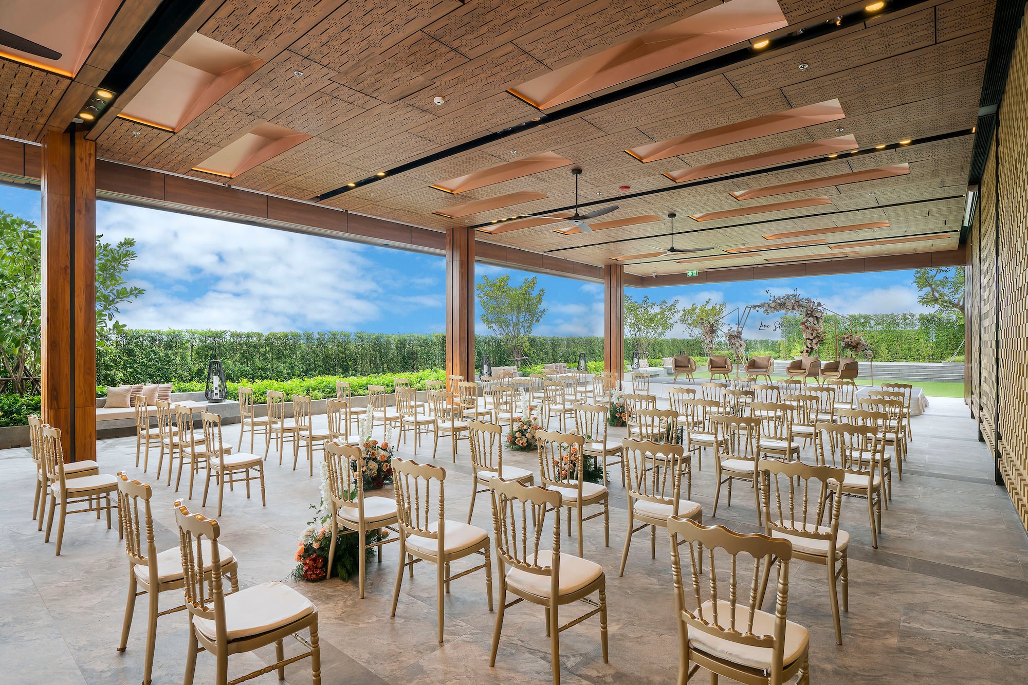 Elegant open-air wedding venue with rows of chairs, floral decor, and garden views.