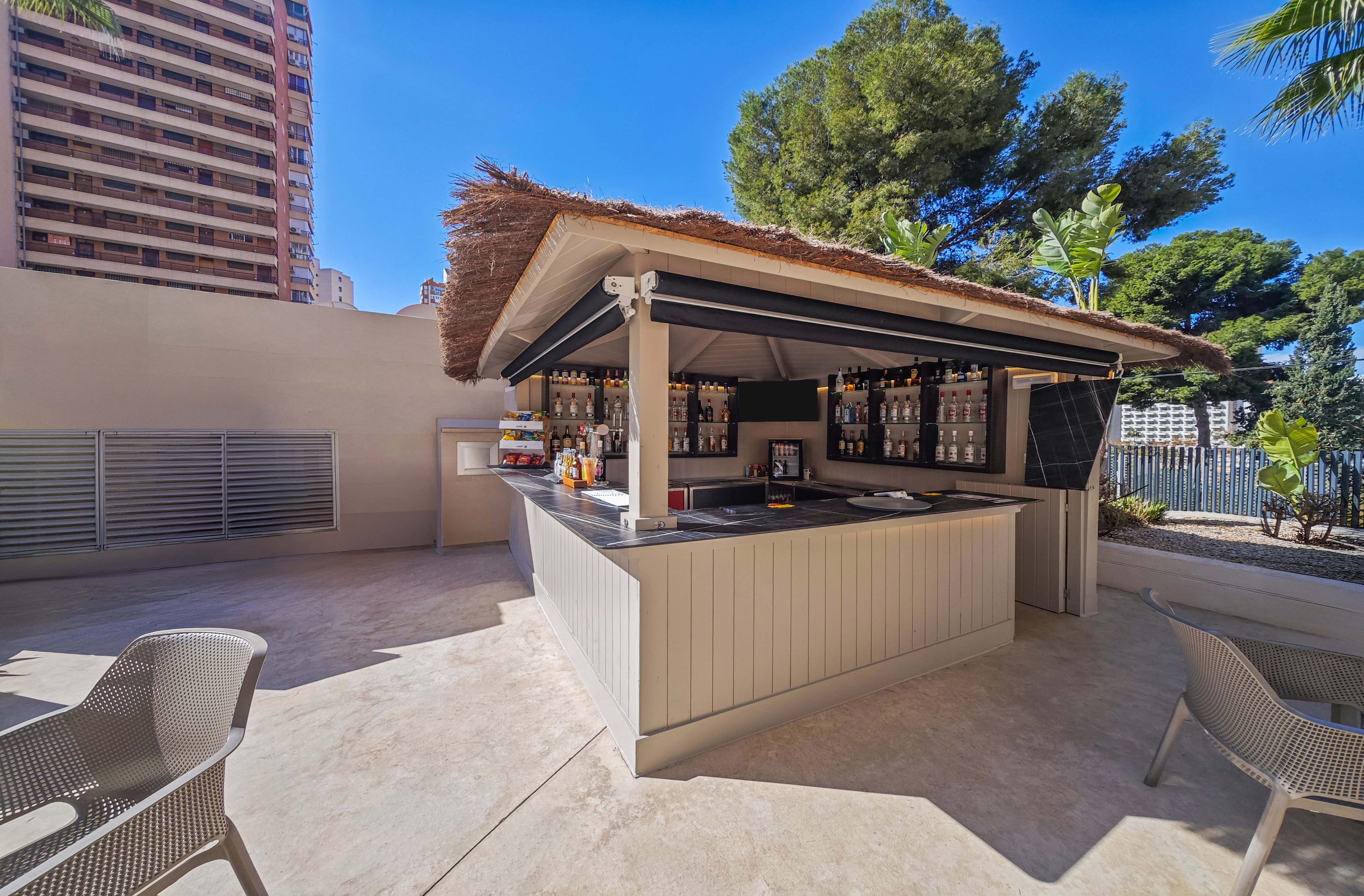 Sunny outdoor resort bar with thatched roof, drinks, and patio seating.