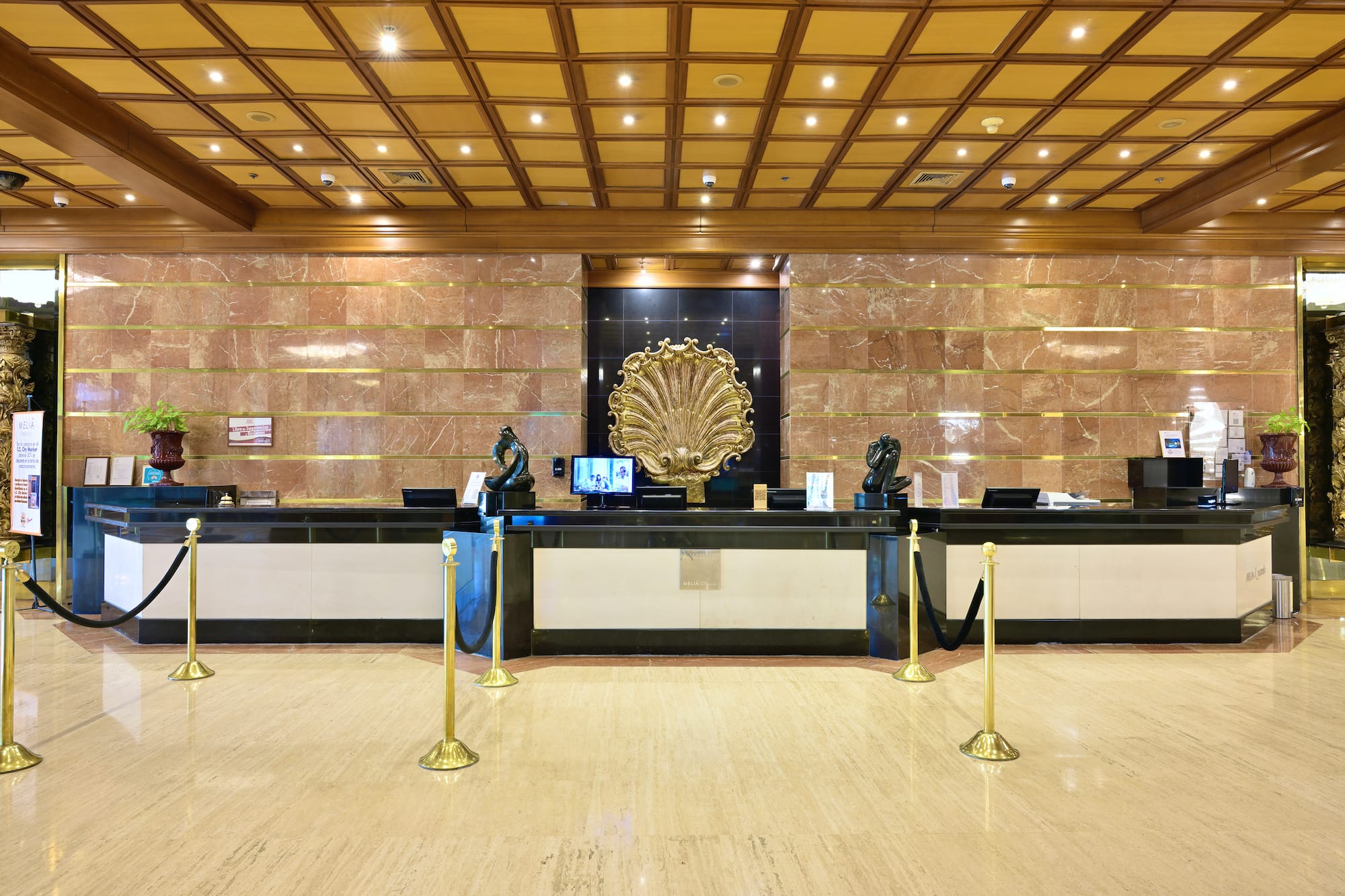 Elegant hotel reception desk with golden shell art, marble walls, and wood ceiling.