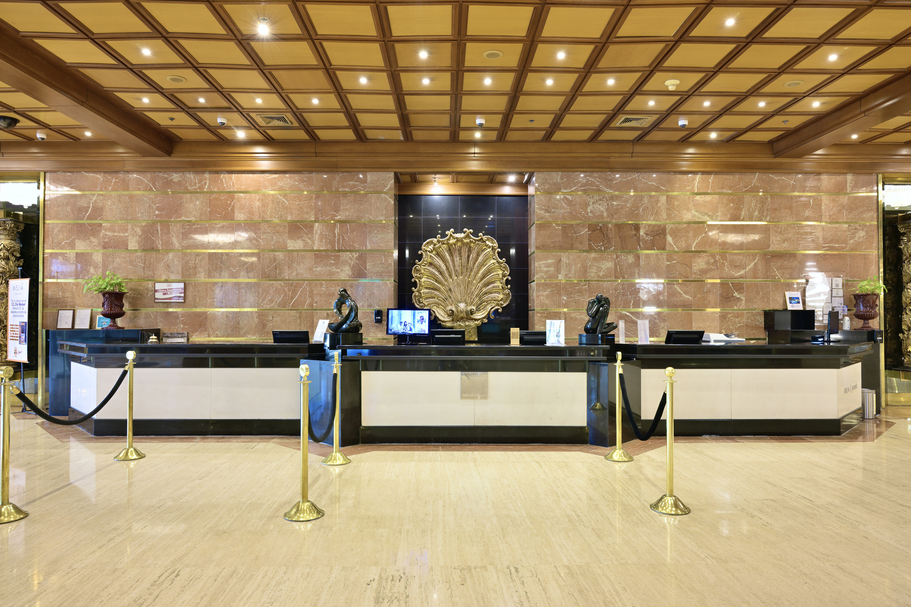 Elegant hotel reception desk with golden shell art, marble walls, and wood ceiling.
