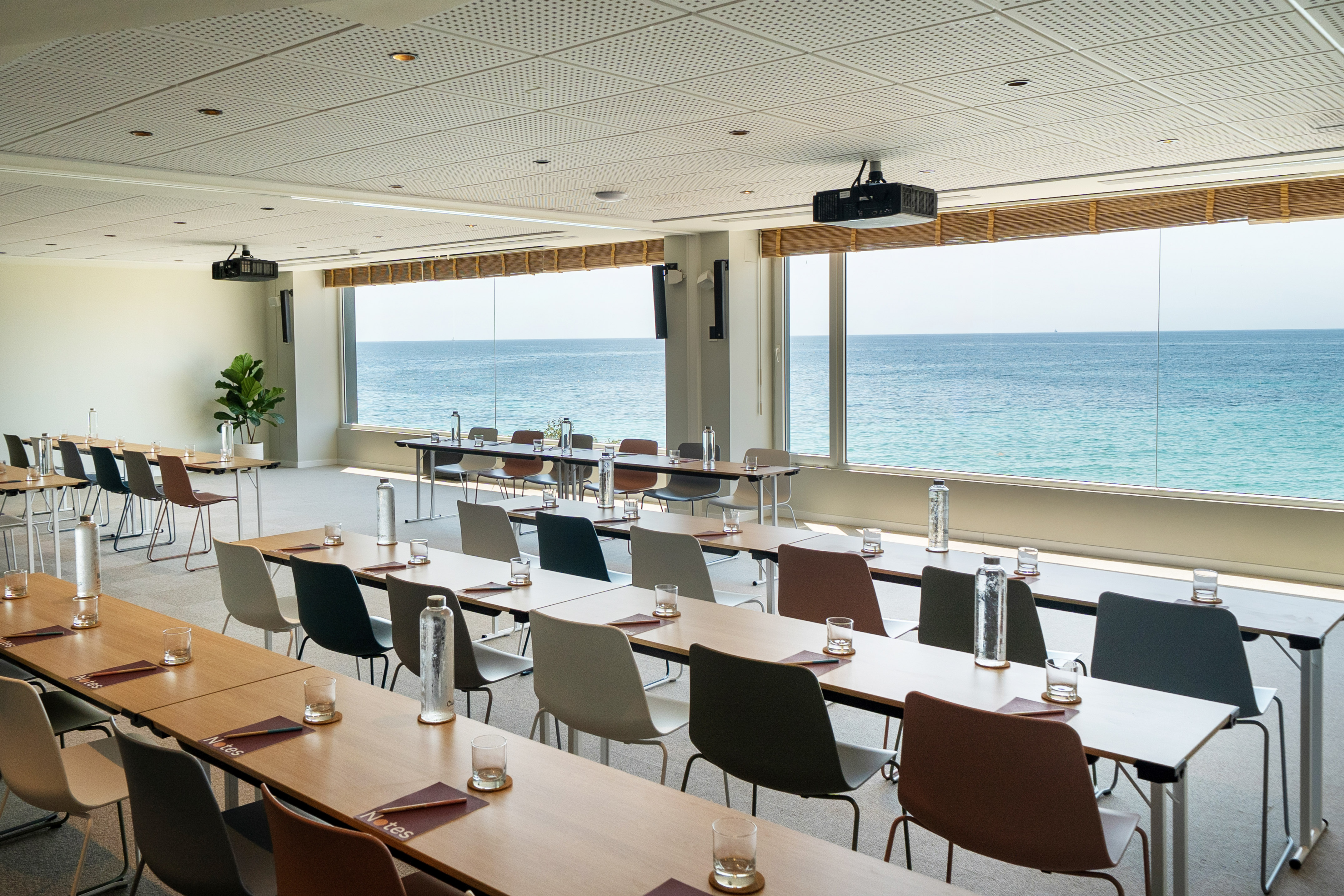 a room with tables and chairs and a large window overlooking the ocean