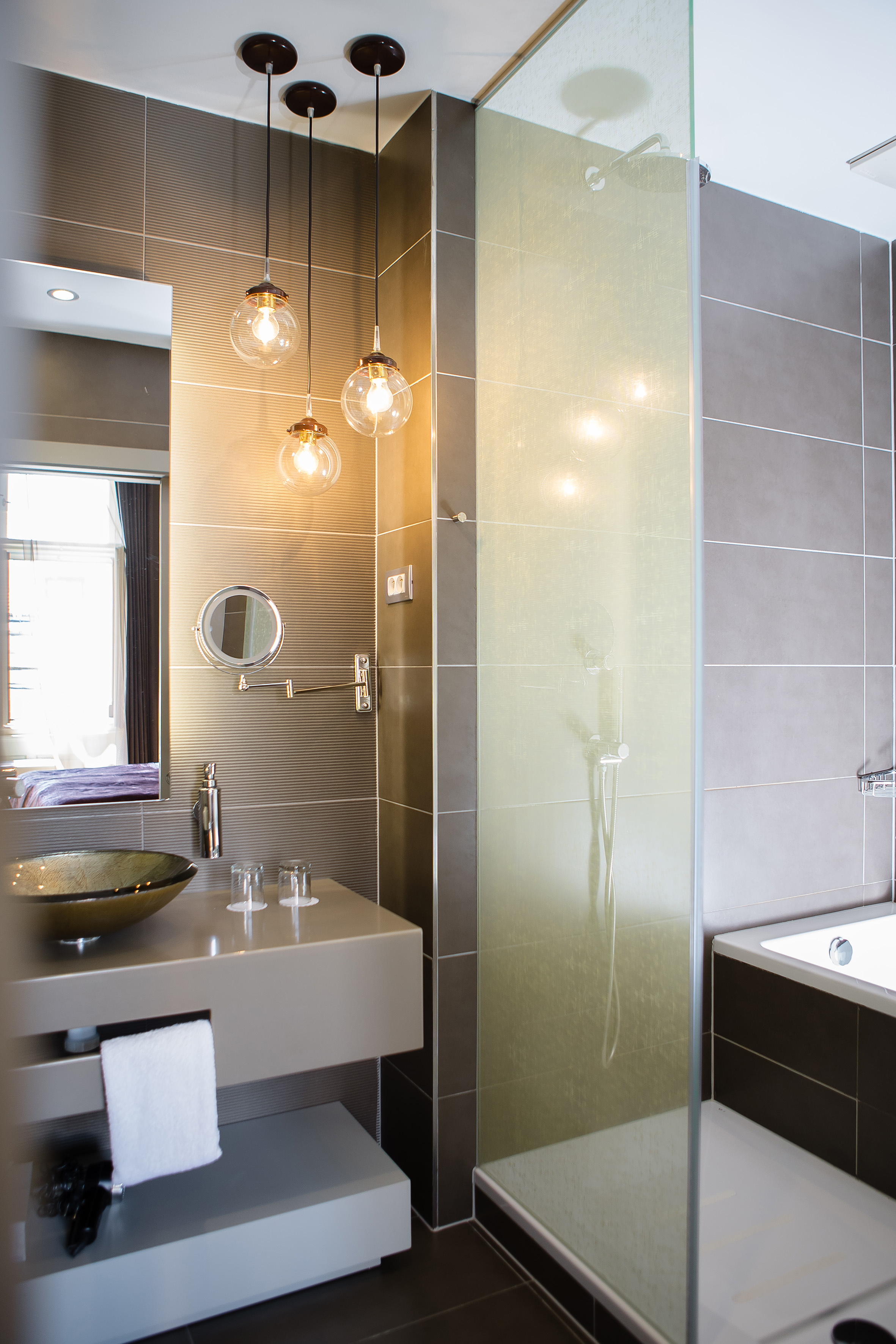 Sleek modern bathroom with vanity, pendant lights, glass shower, and tub.