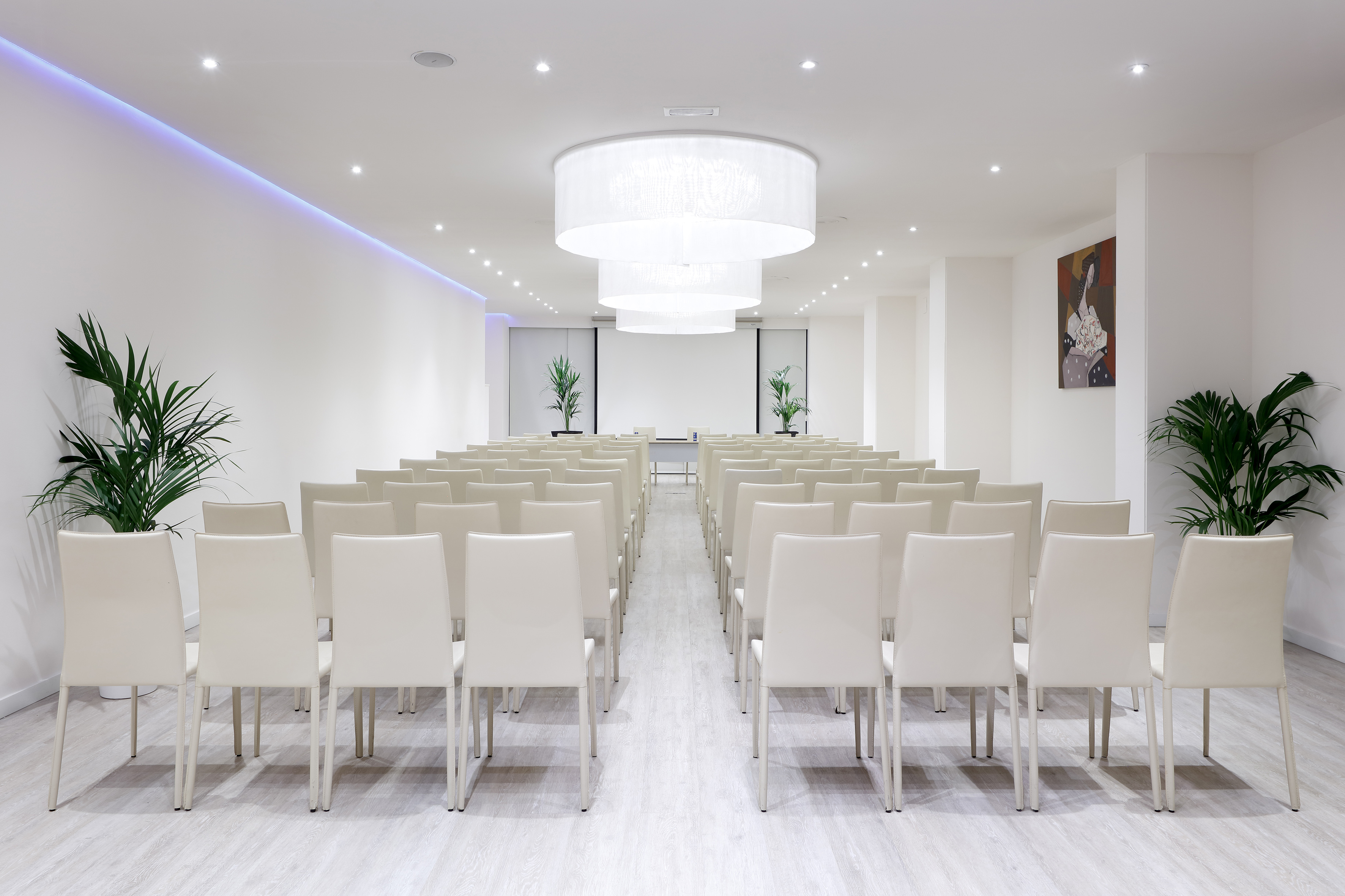 Modern conference room with rows of chairs, projection screen, and elegant chandeliers.