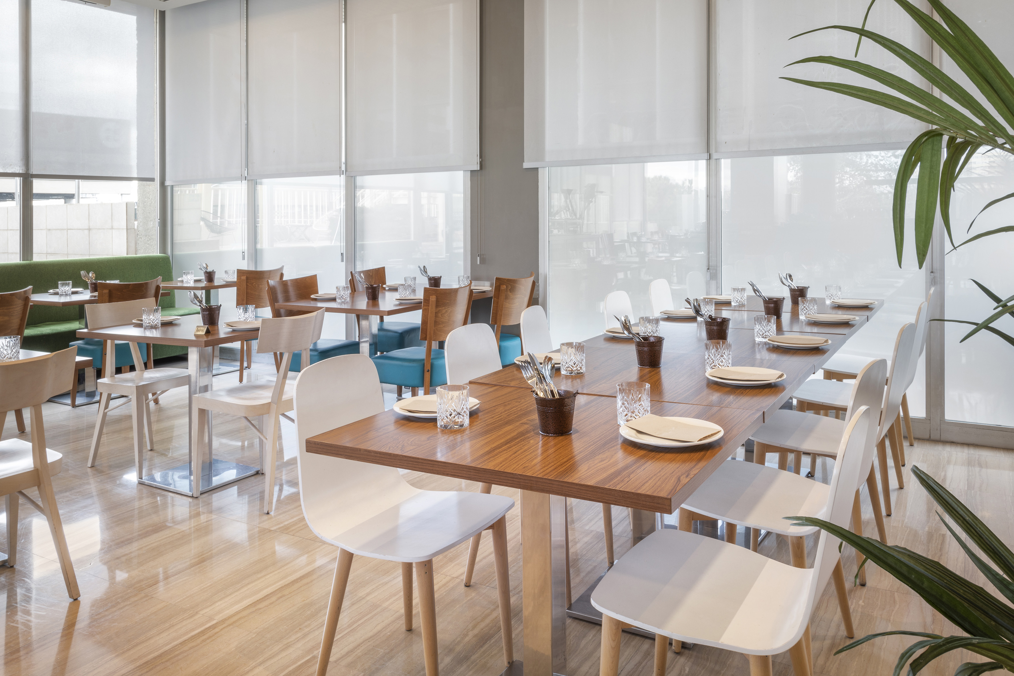 Bright modern restaurant dining room with set tables, white chairs, large windows.