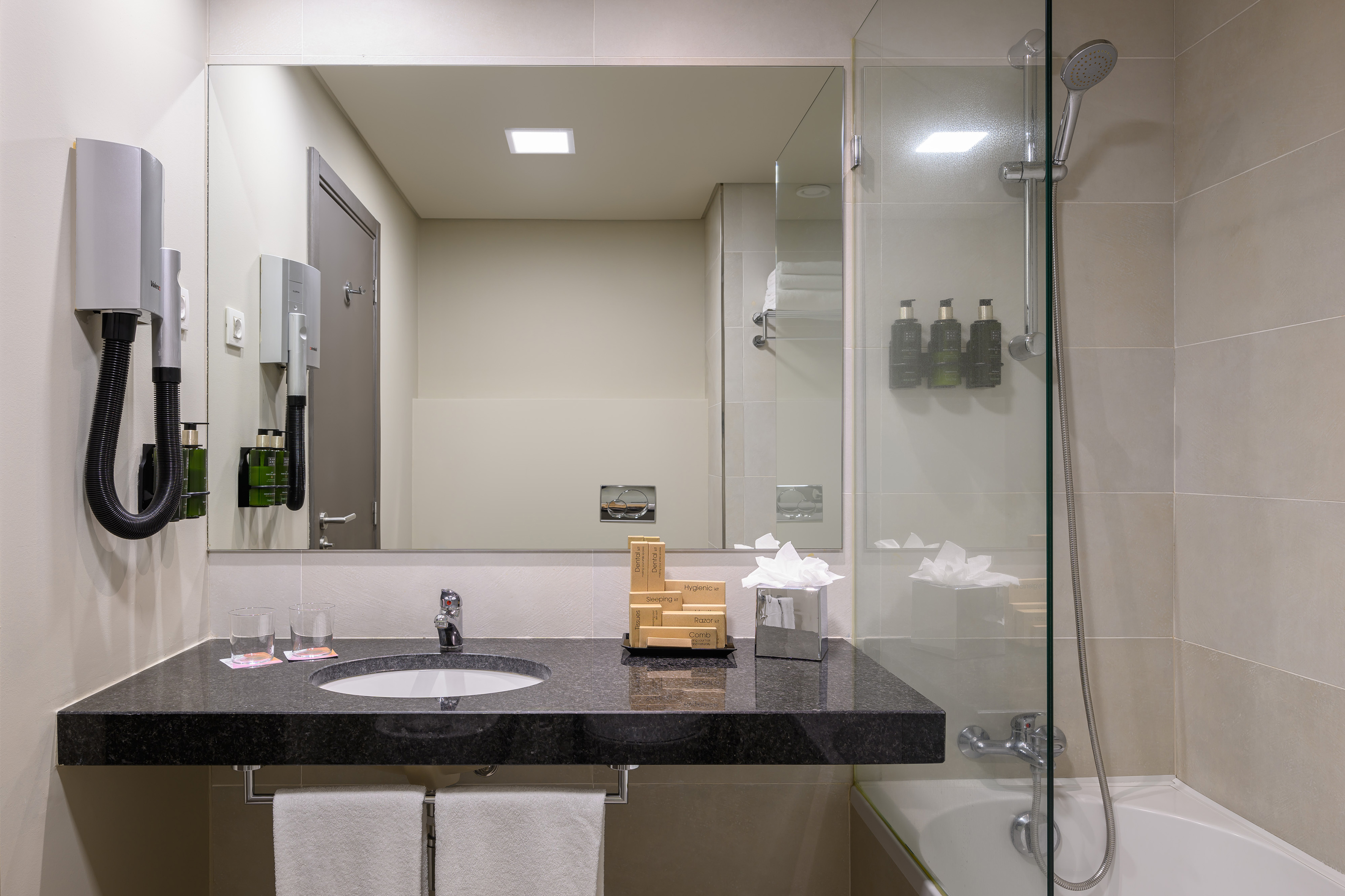 Hotel bathroom with granite vanity, sink, mirror, wall dryer, shower, and tub.