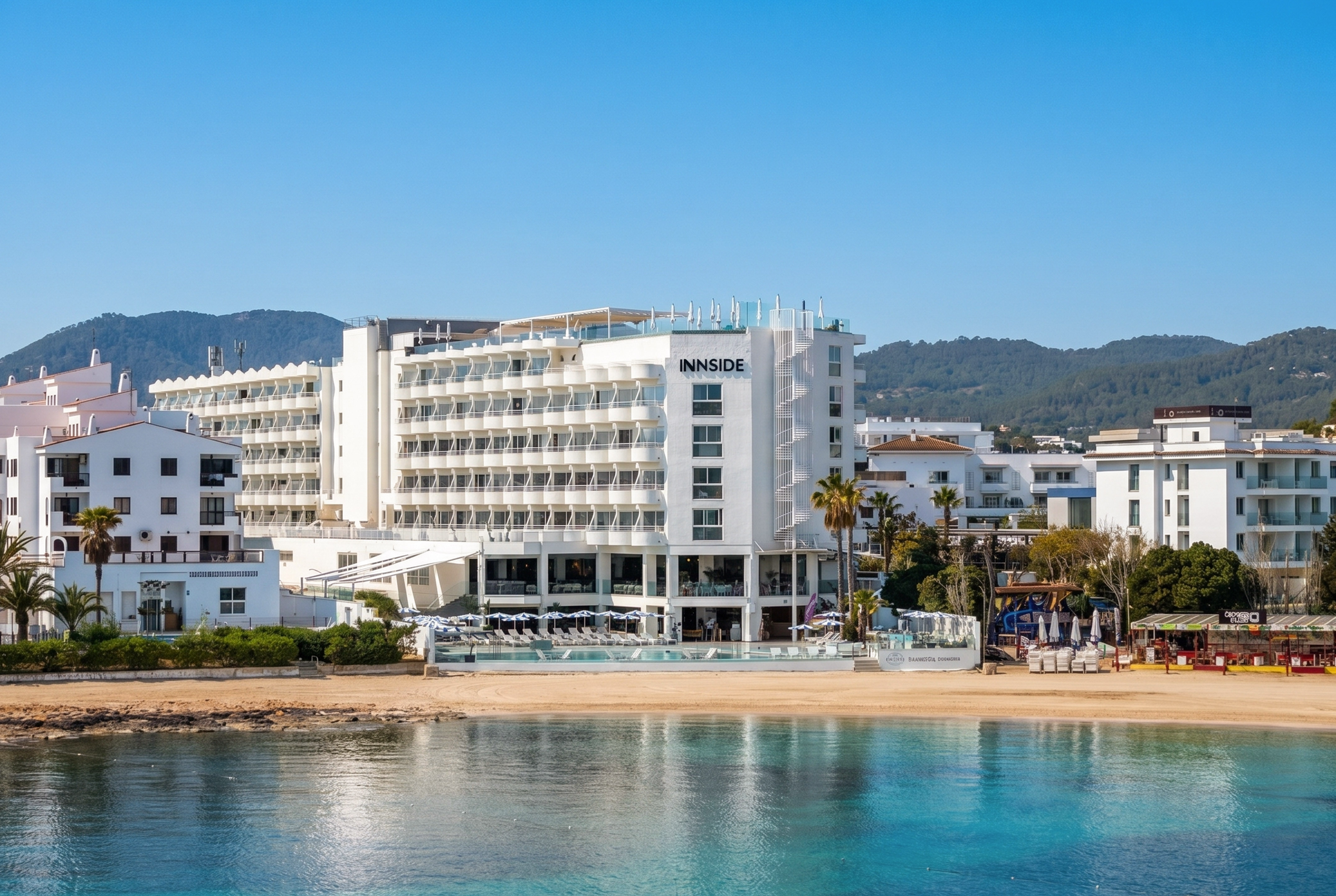 INNSIDE beach hotel on a sunny coast with turquoise water and green hills.