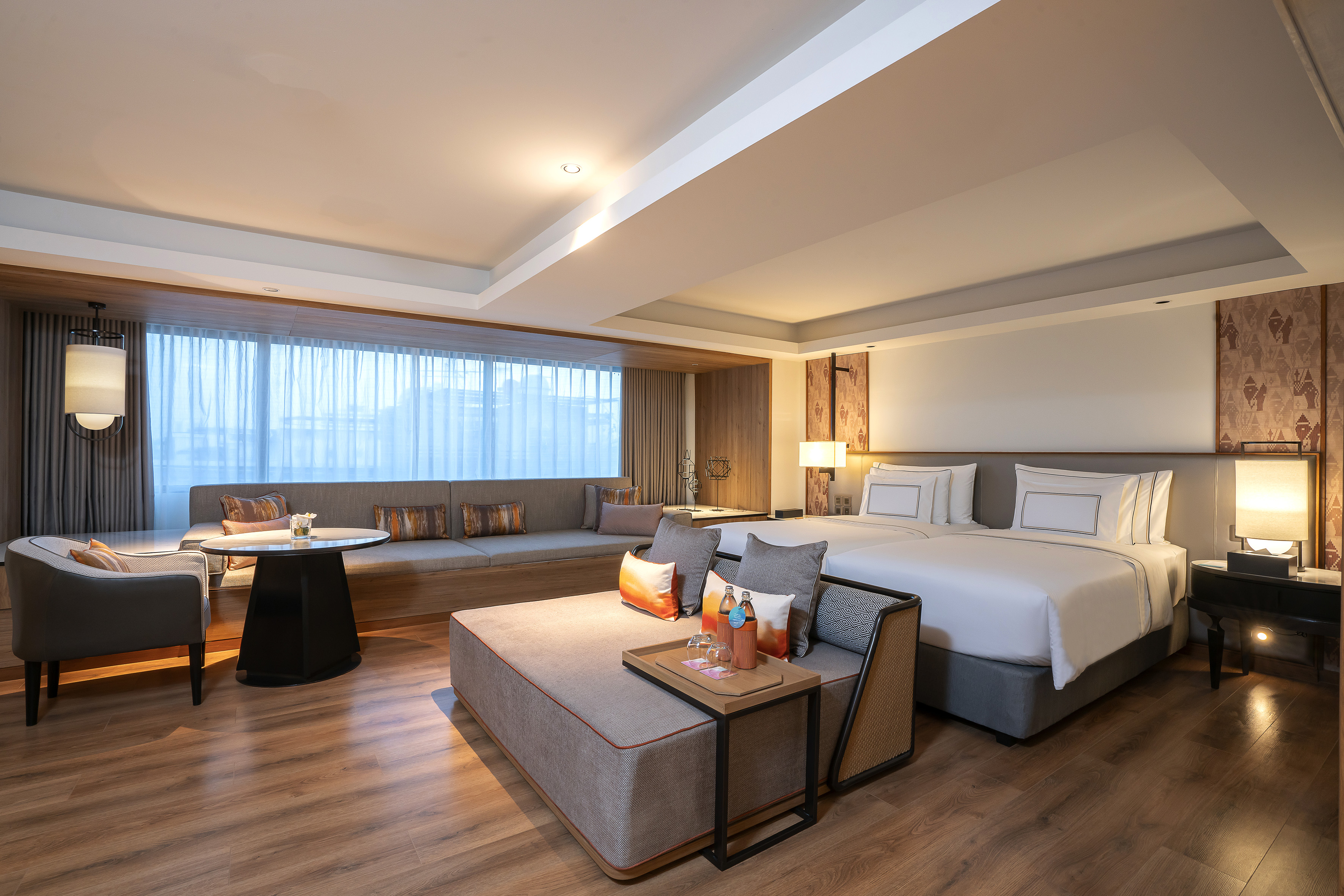 Modern hotel suite with twin beds, lounge area, and hardwood floor.