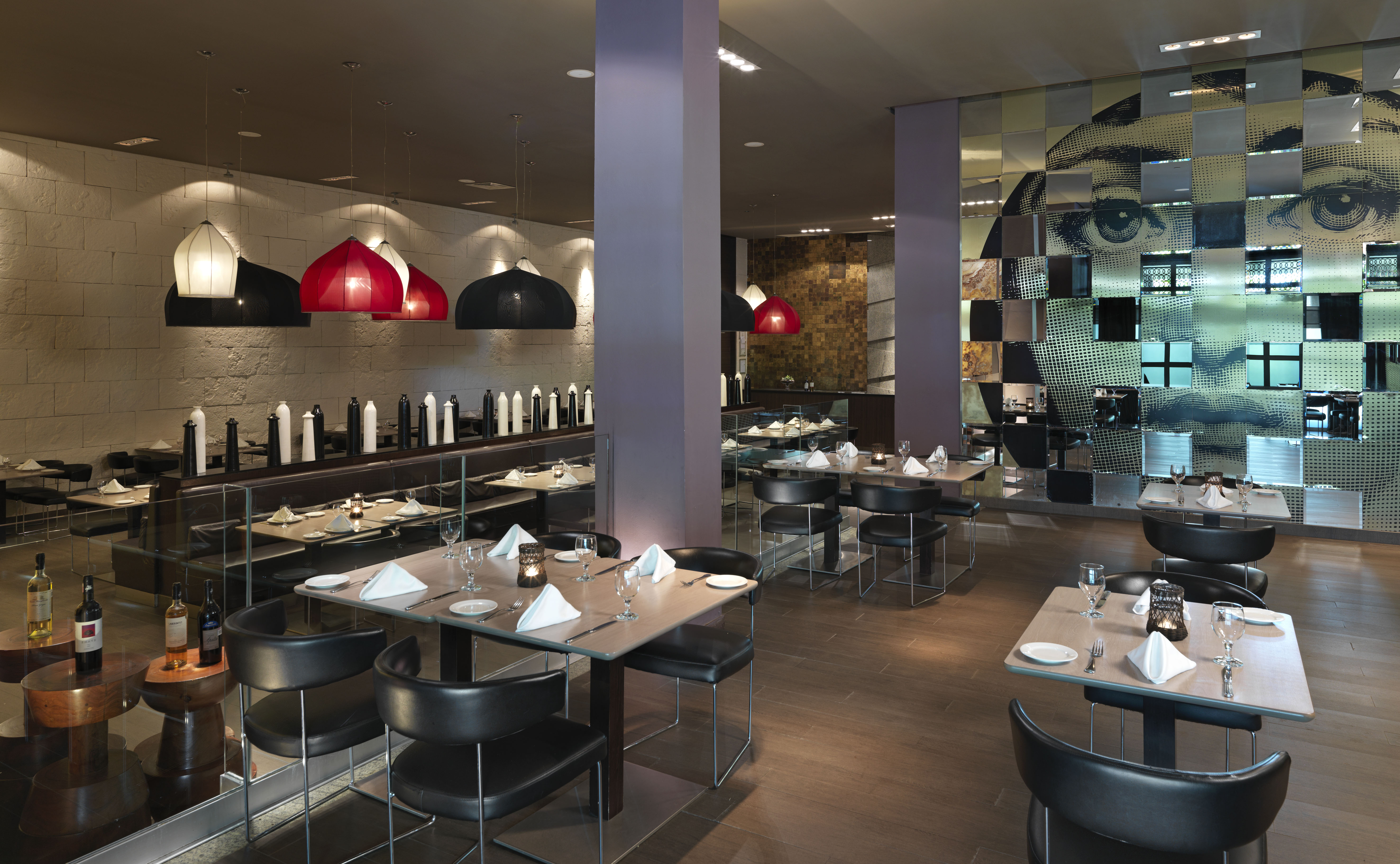 Contemporary restaurant with set tables, modern pendant lights, and a mirrored face mural.