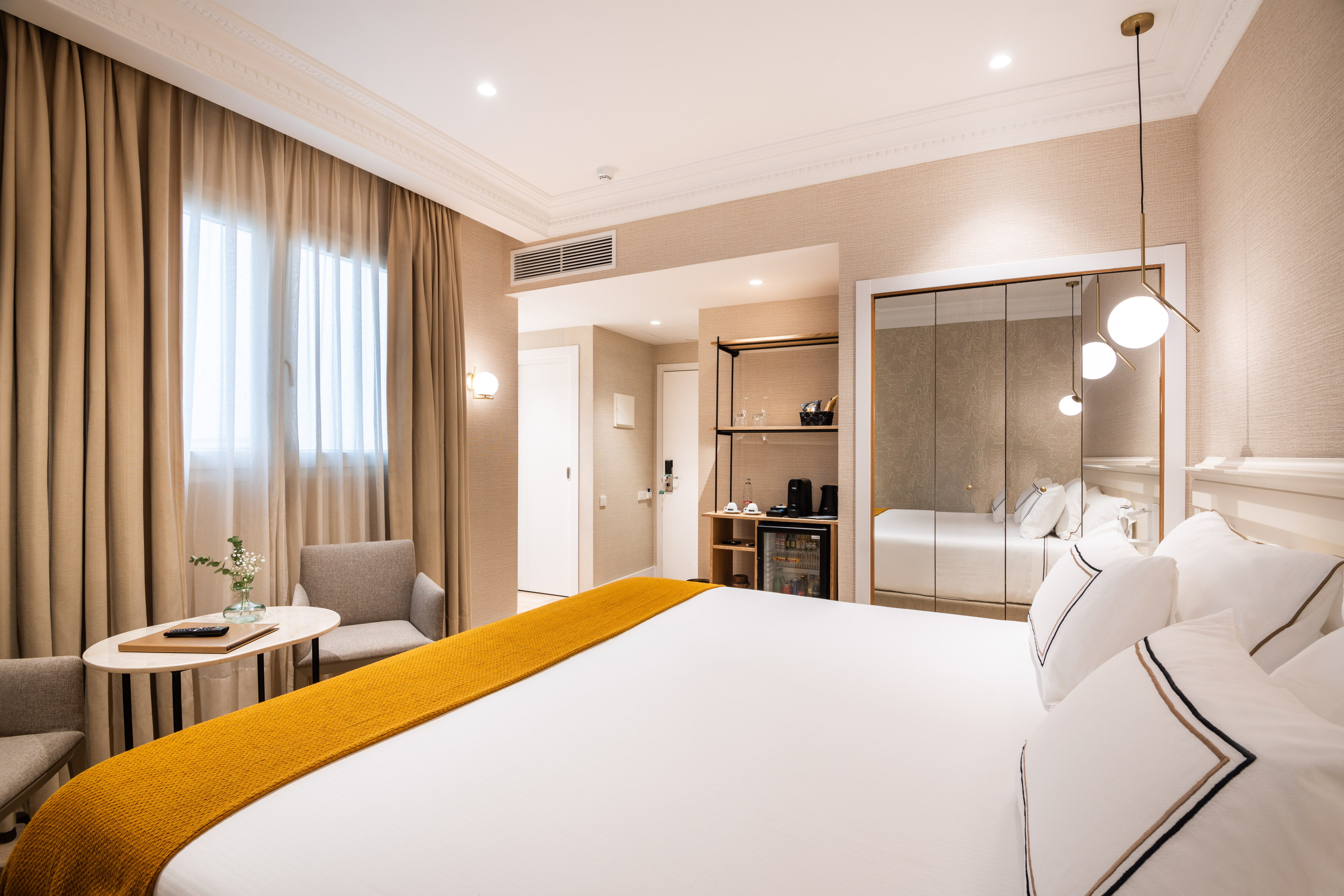 Contemporary hotel room with bed, yellow blanket, window, and minibar.