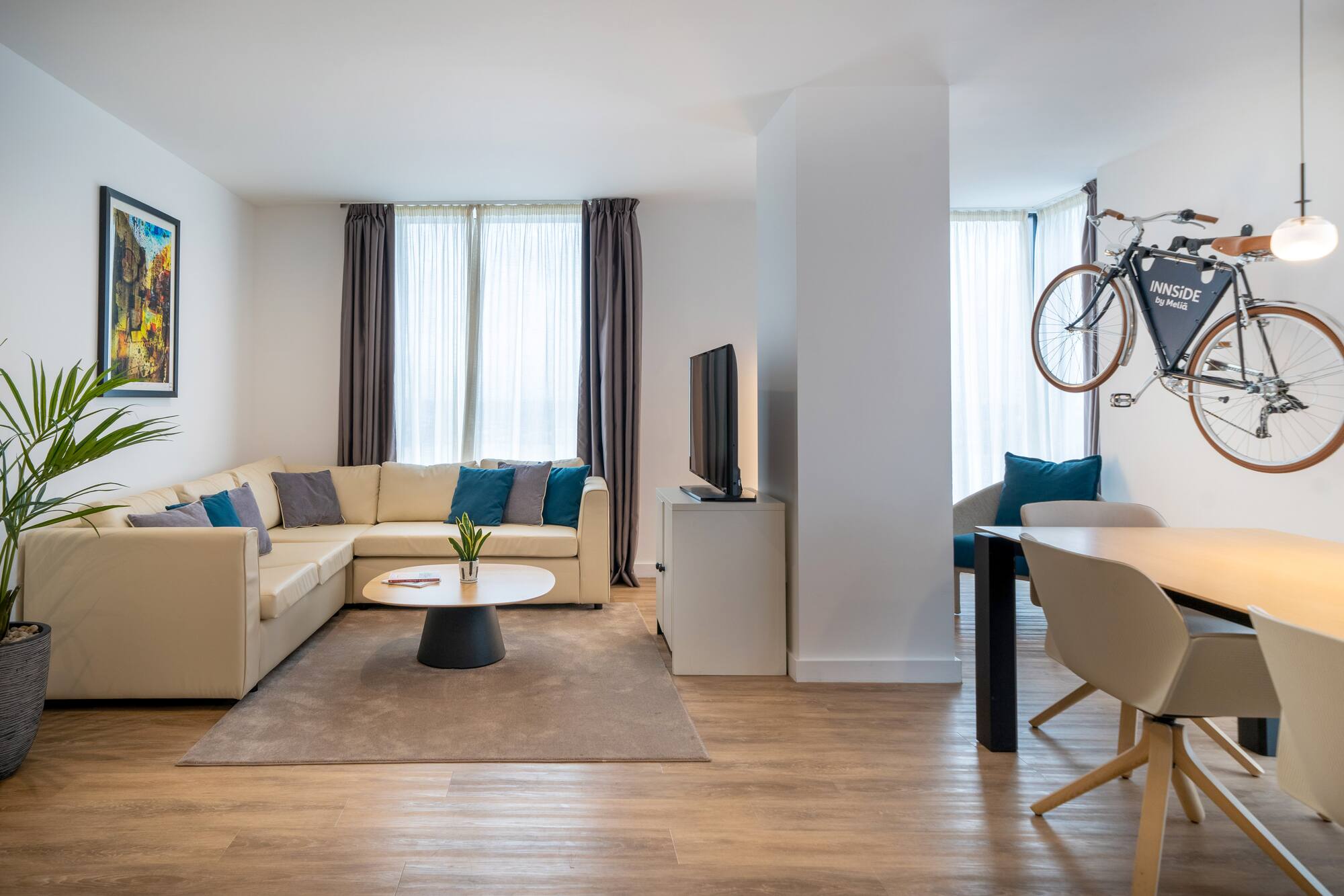 Modern hotel suite living room with beige sofa, dining area, and bicycle decor.