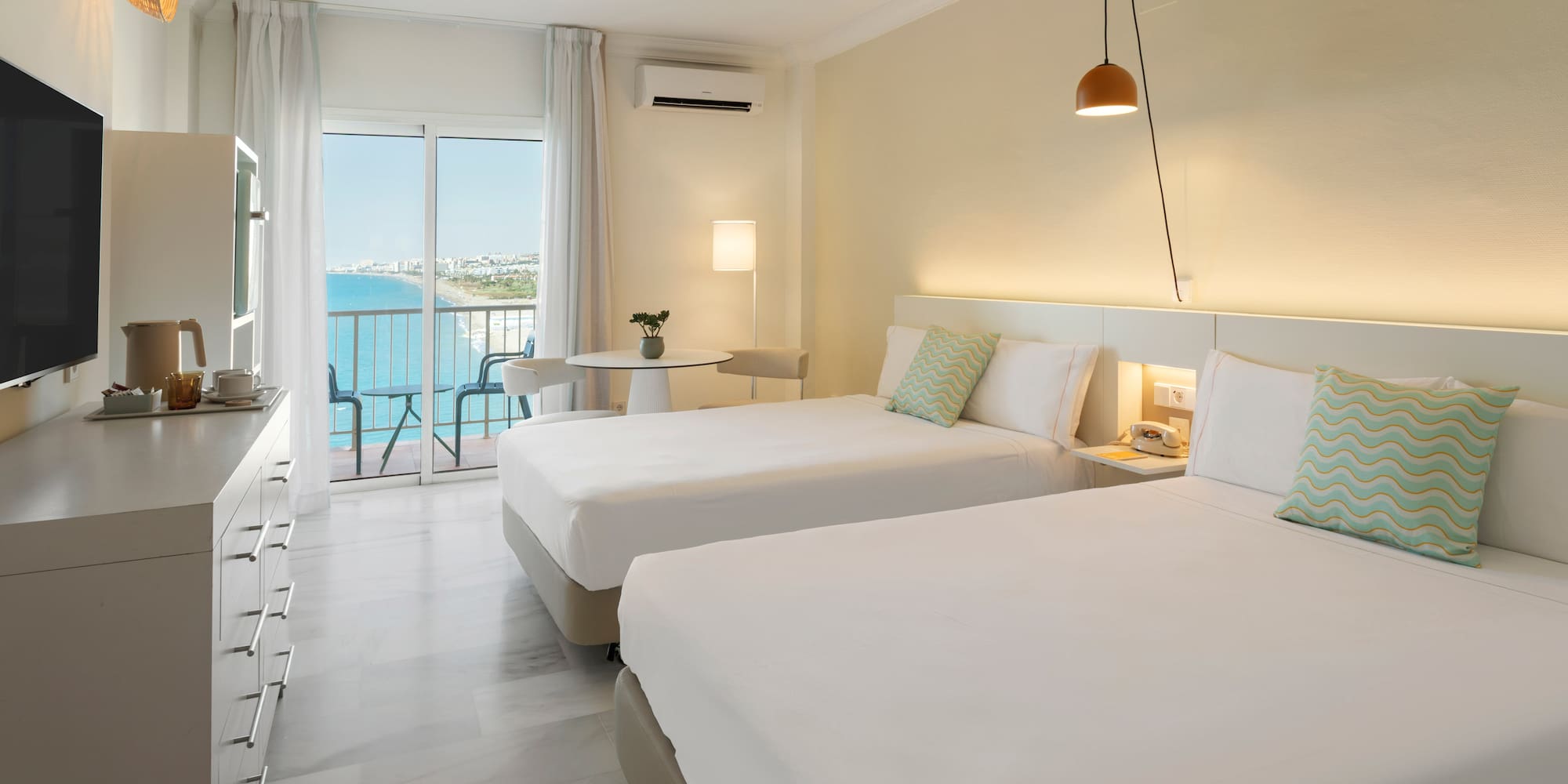 Coastal hotel room with twin beds, balcony sea view, and contemporary design.