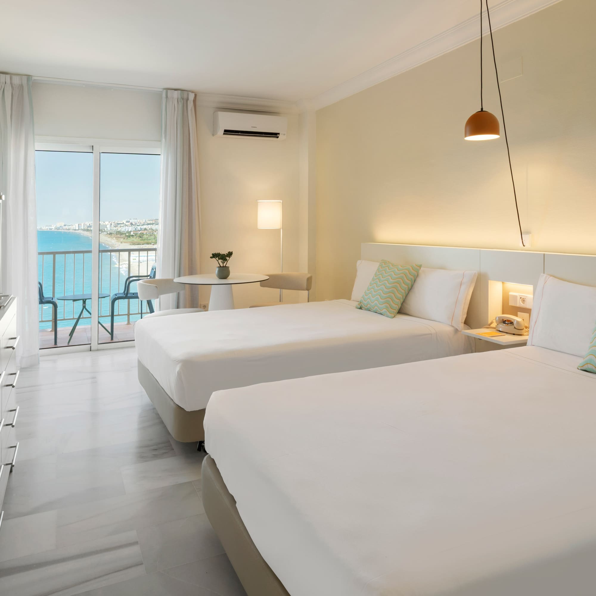 Coastal hotel room with twin beds, balcony sea view, and contemporary design.