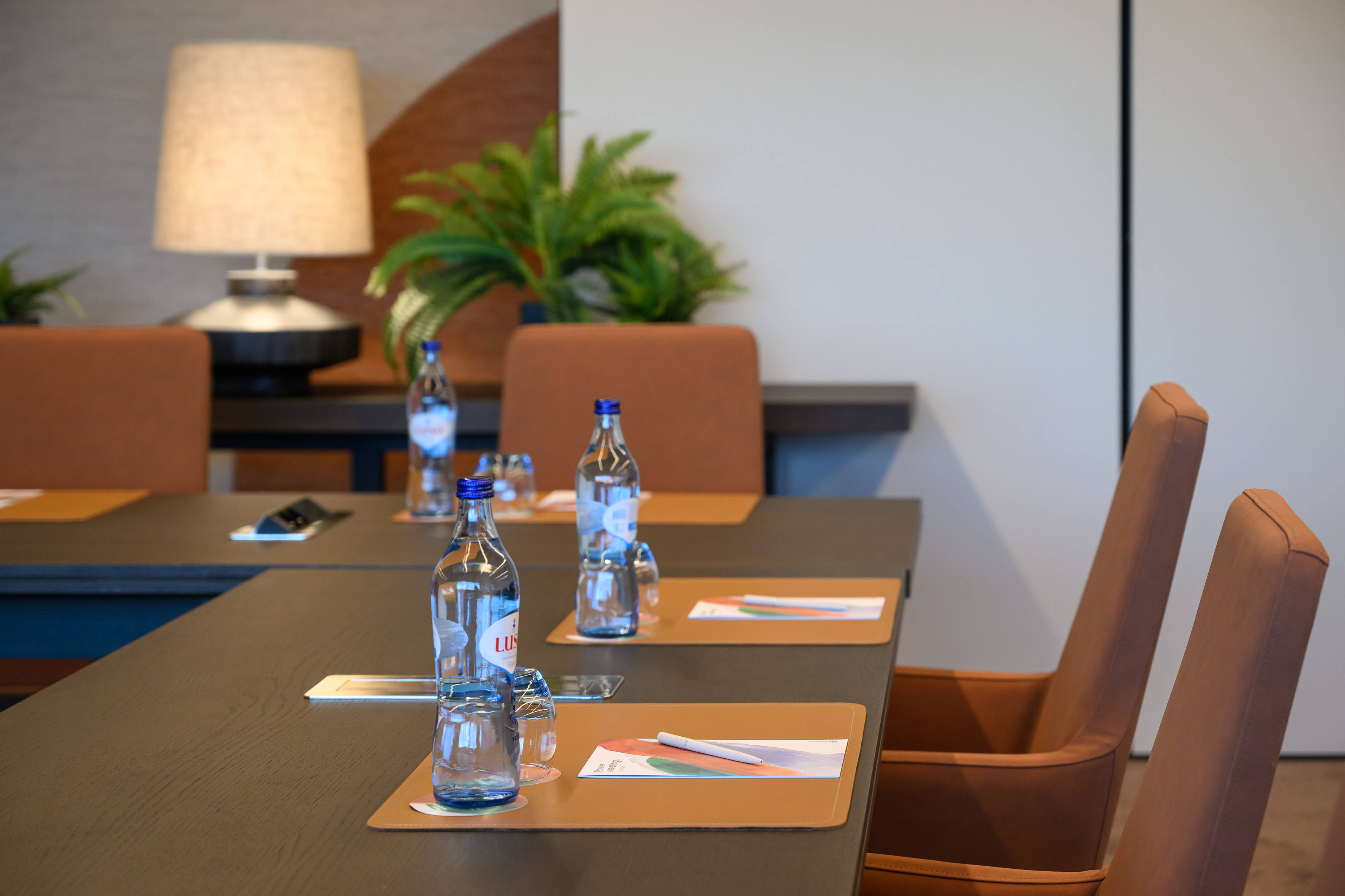 Modern meeting room: dark table, brown chairs, water, and notebooks.