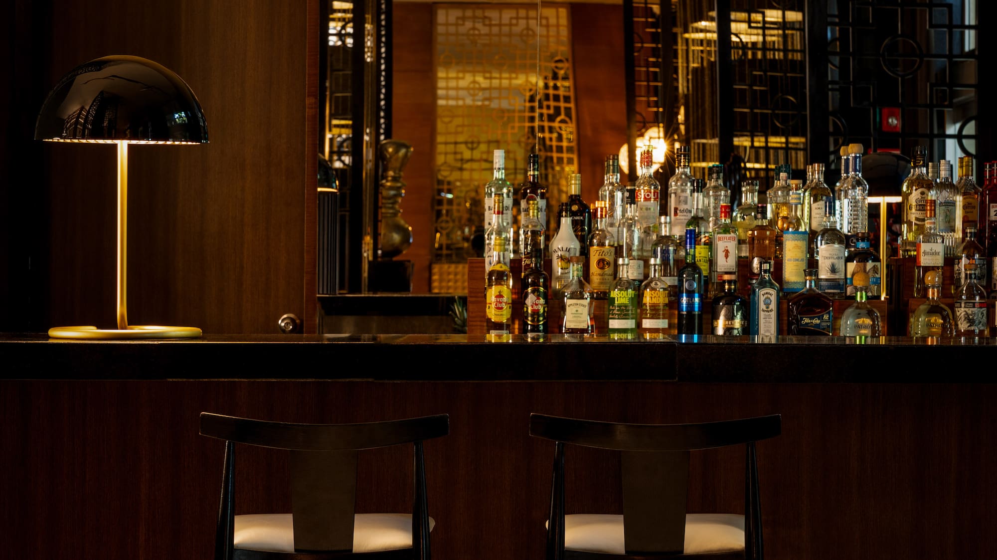 Upscale dark wood bar with liquor bottles, modern lamp, and two bar stools.