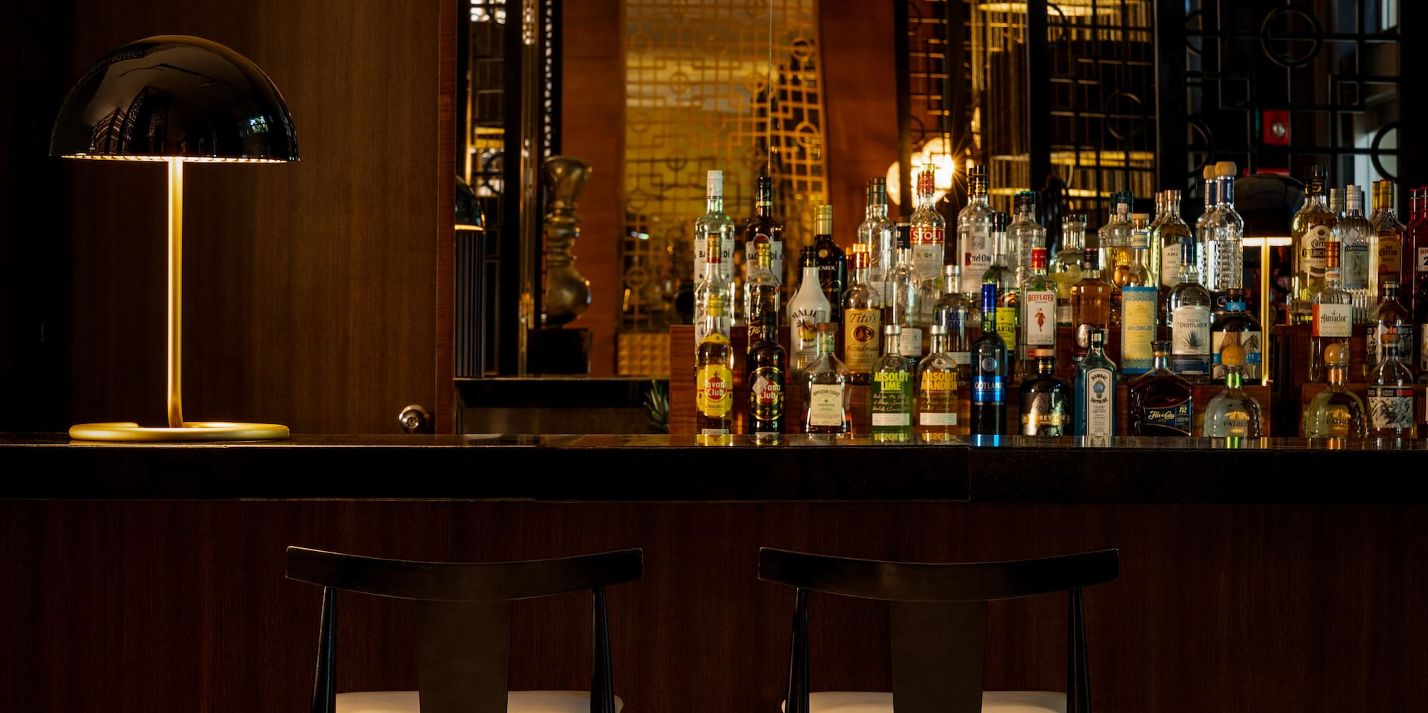 Upscale dark wood bar with liquor bottles, modern lamp, and two bar stools.