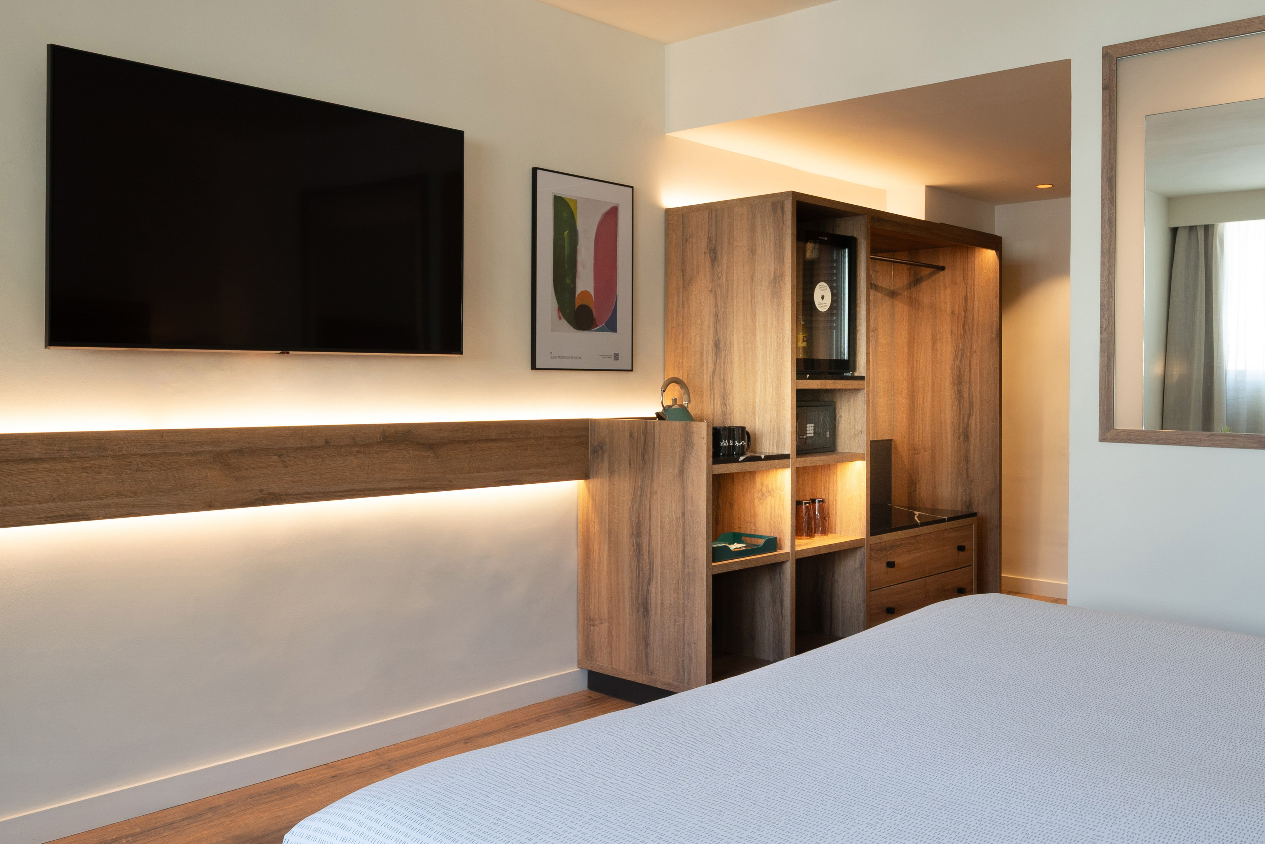Modern hotel room with TV, wooden storage, minibar, and ambient lighting.