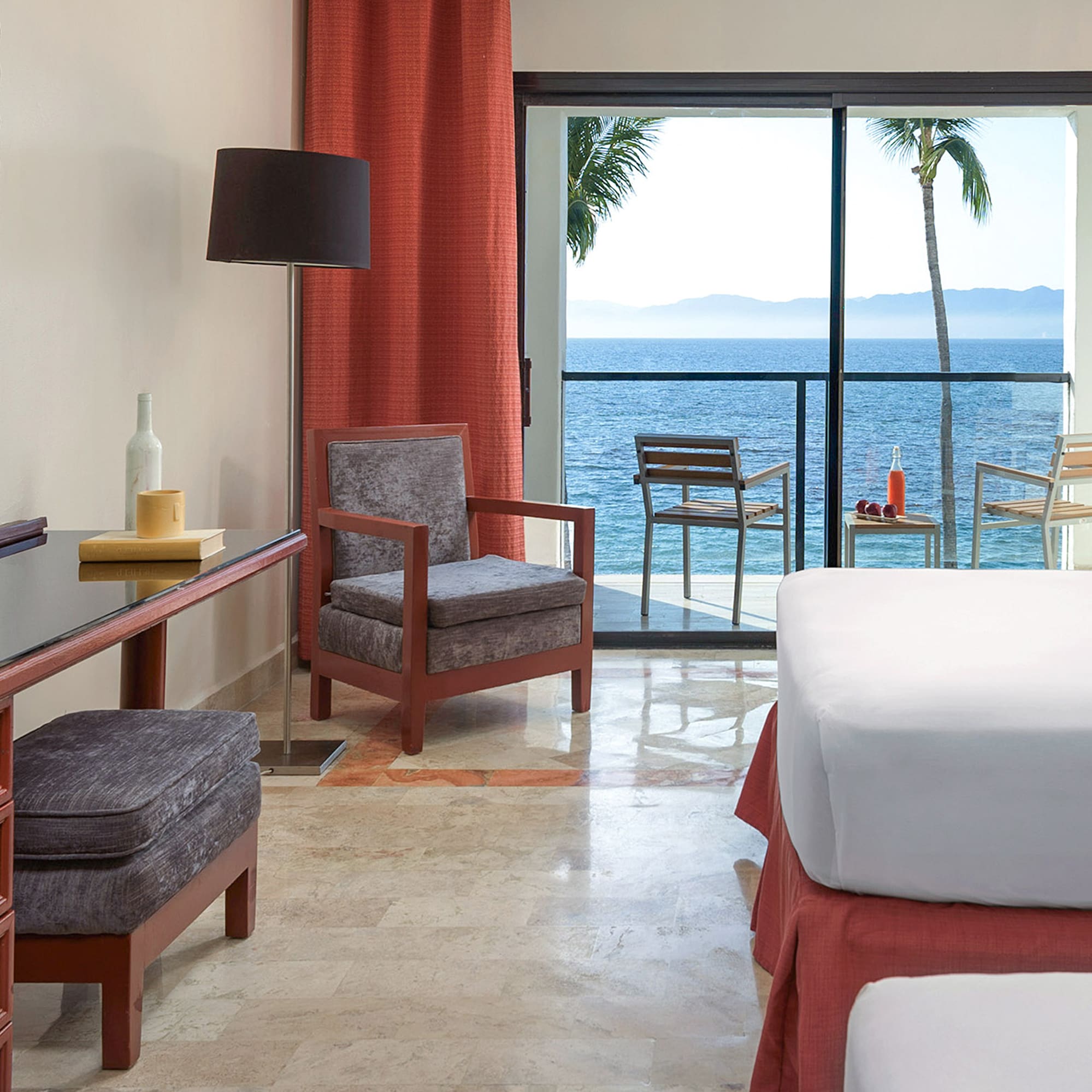 a room with a bed and chairs and a table with a view of the ocean