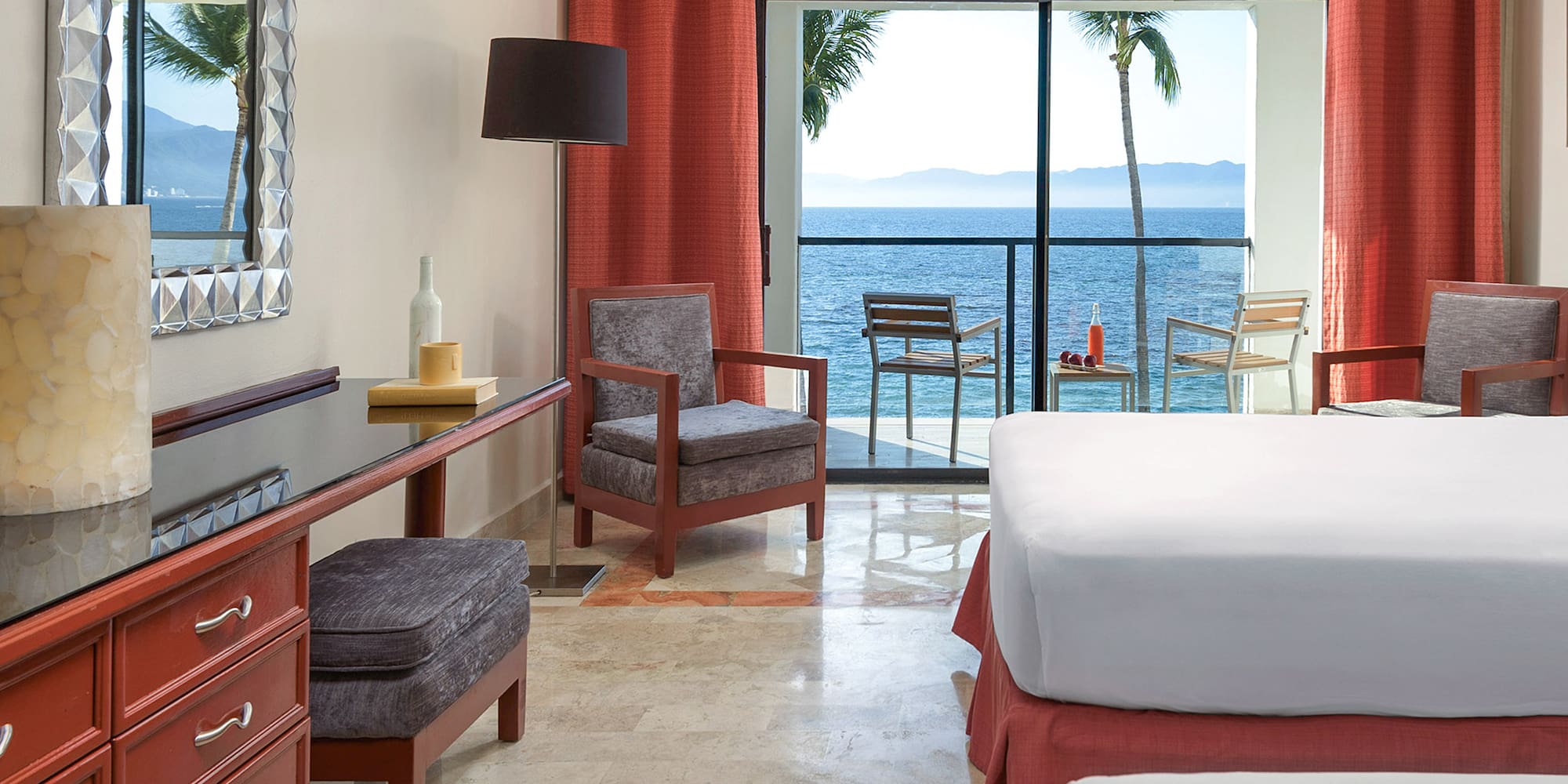 a room with a bed and chairs and a table with a view of the ocean