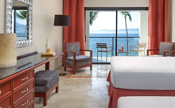 a room with a bed and chairs and a table with a view of the ocean