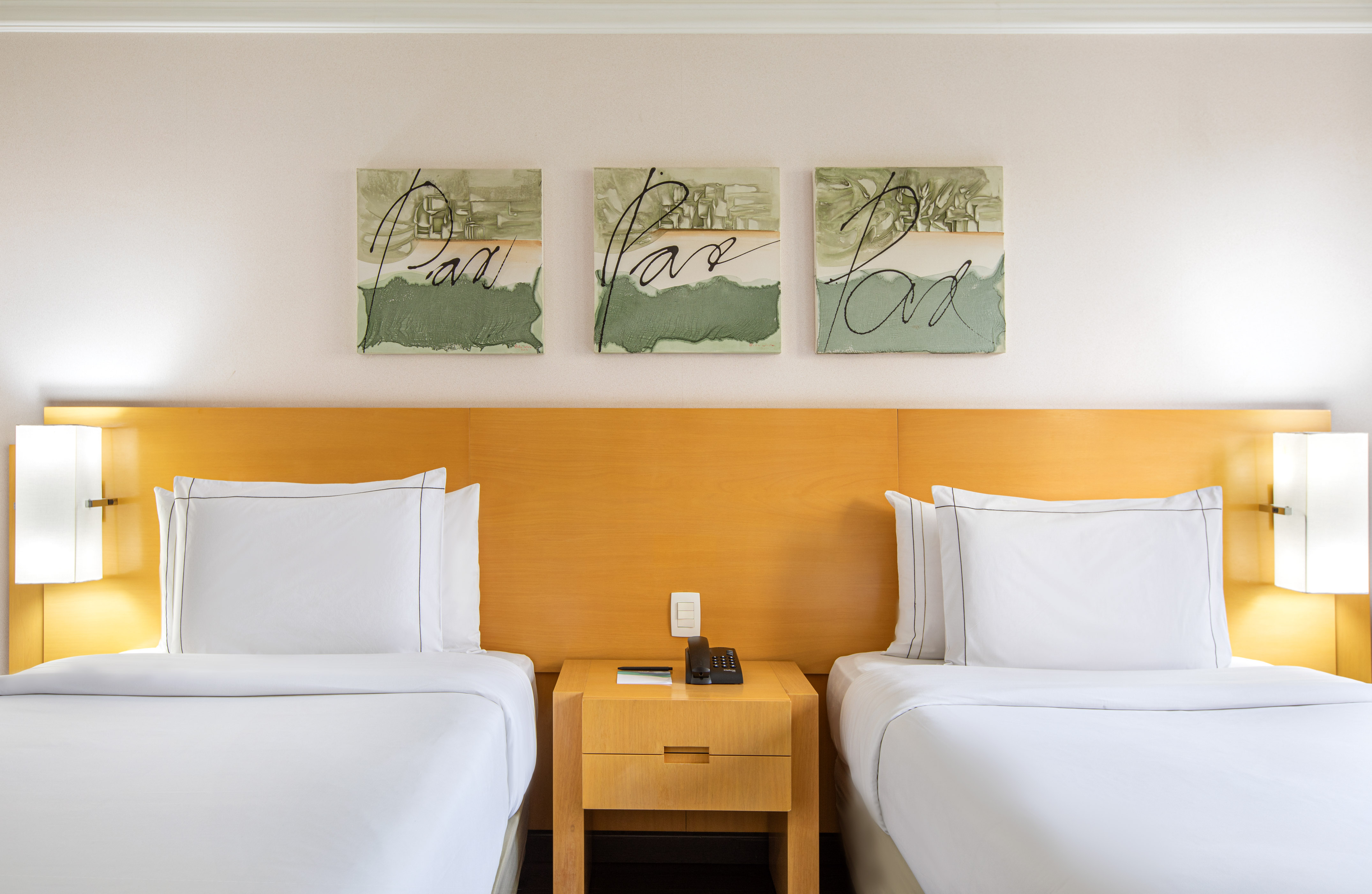 Modern hotel room with two beds, white linen, wooden headboard, and abstract wall art.