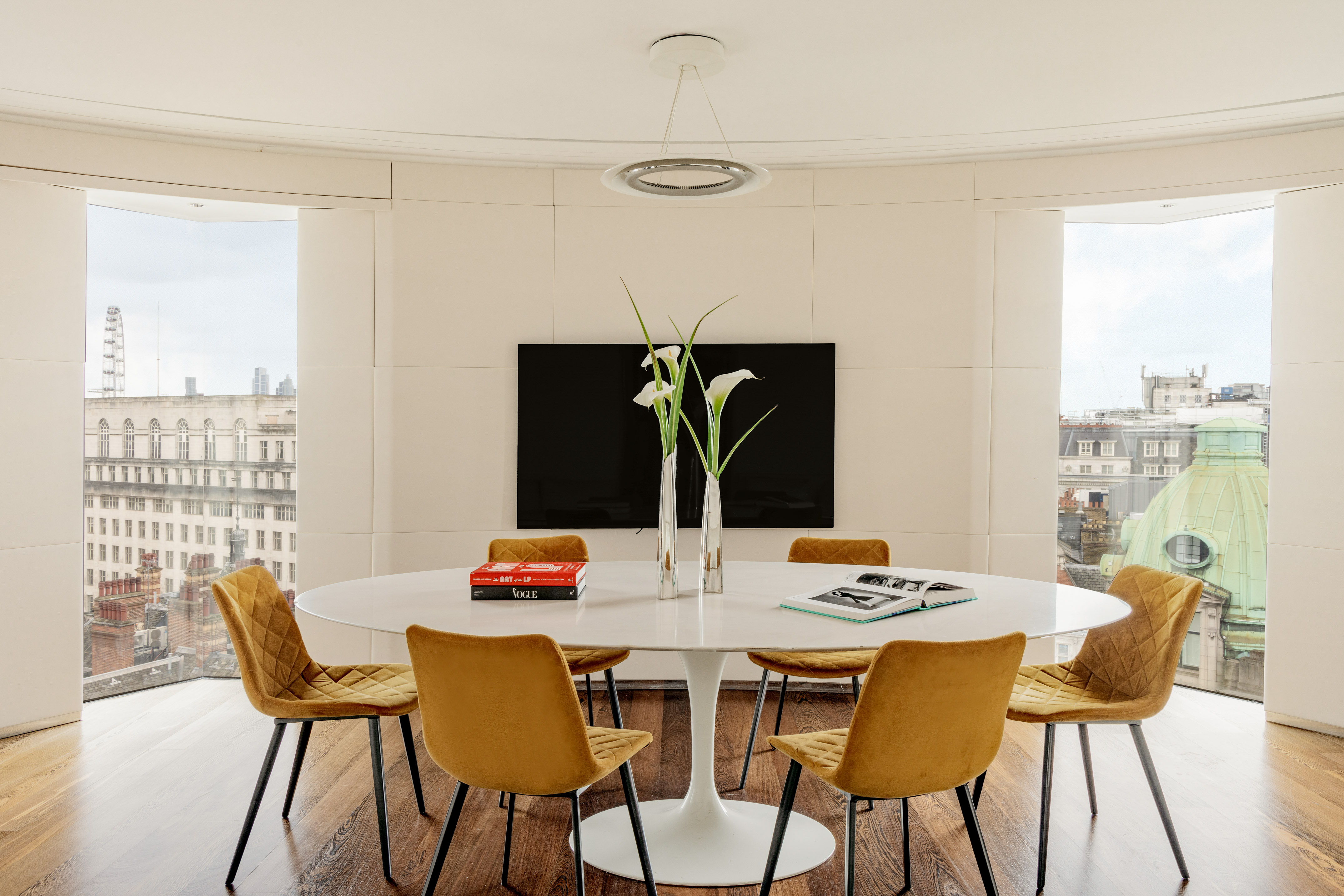 Modern dining room with white tulip table, yellow chairs, and city view.