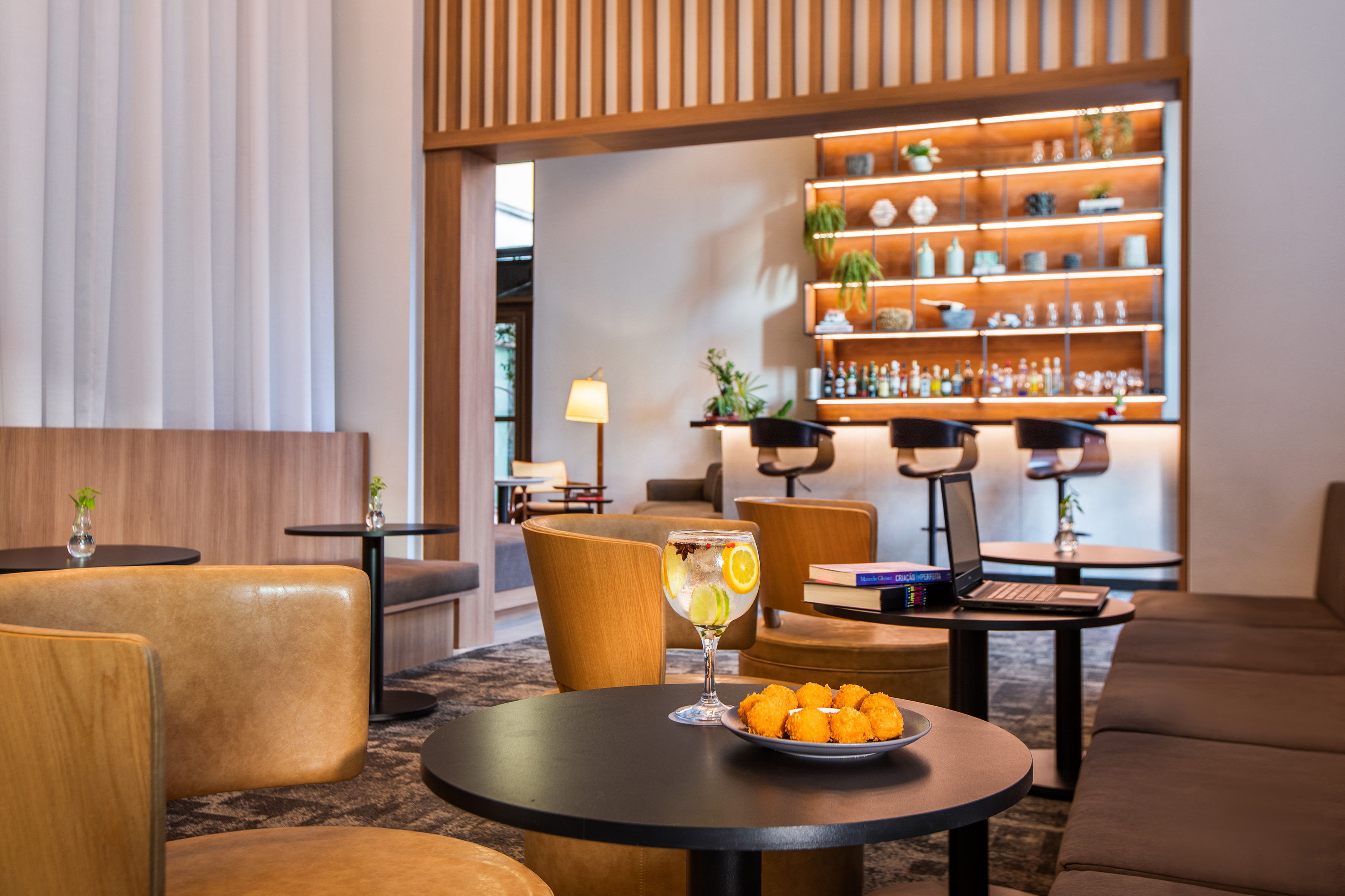 Modern hotel lounge bar with gin & tonic, snacks, and laptop on a table.