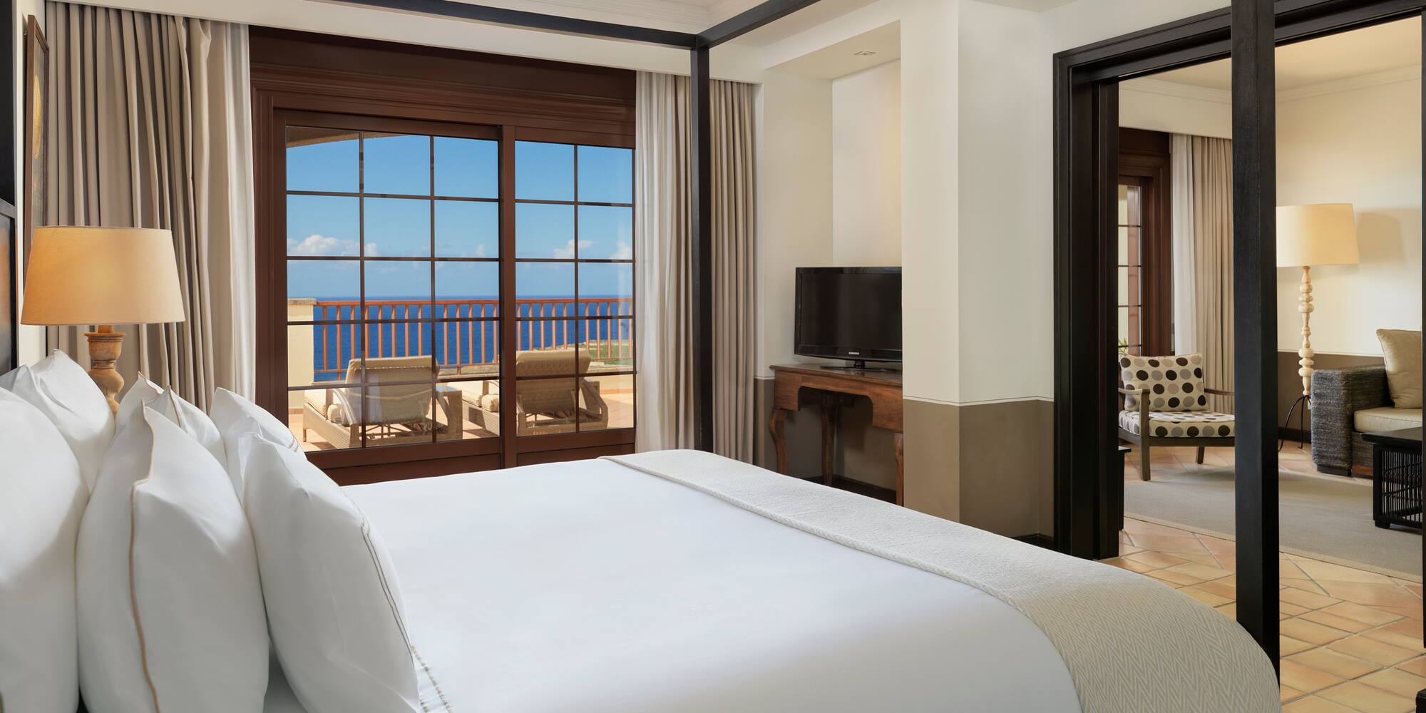 a bed with white sheets and a mirror in a room with a view of the ocean