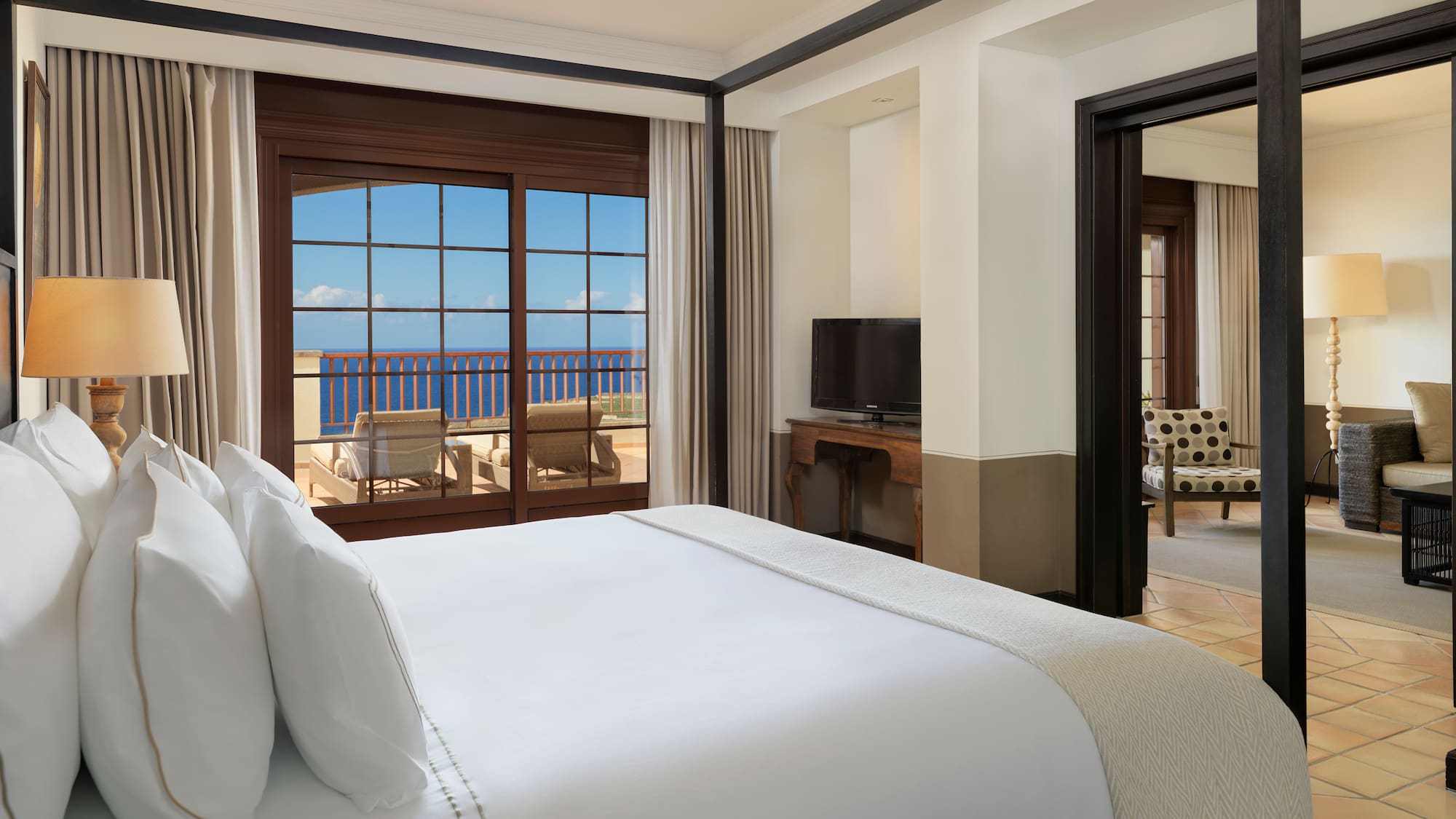 a bed with white sheets and a mirror in a room with a view of the ocean