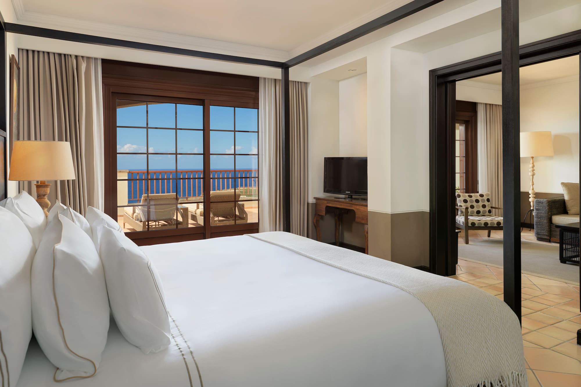 a bed with white sheets and a mirror in a room with a view of the ocean